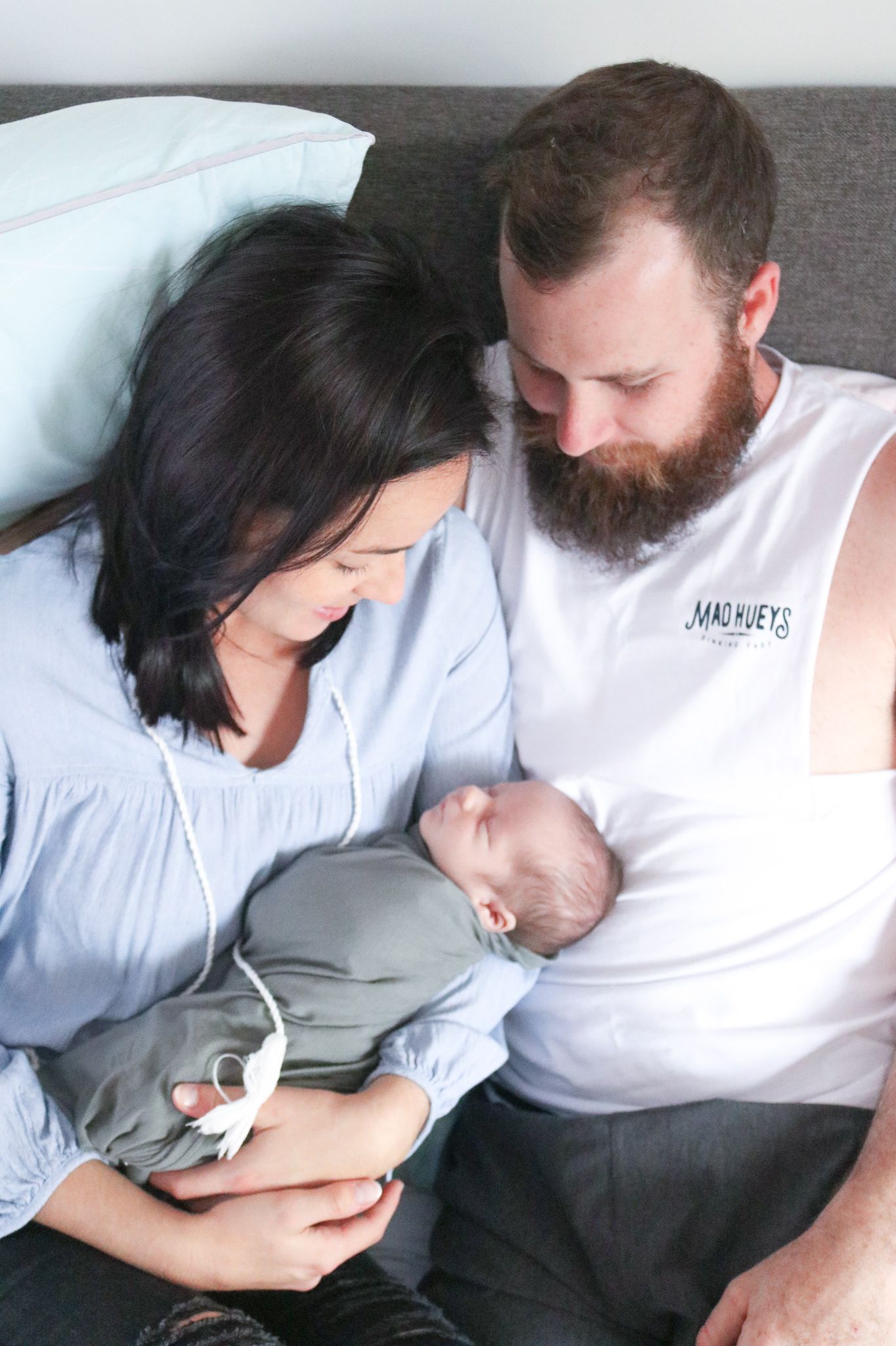 A couple lovingly gazes at their newborn baby while sitting together on a gray couch.