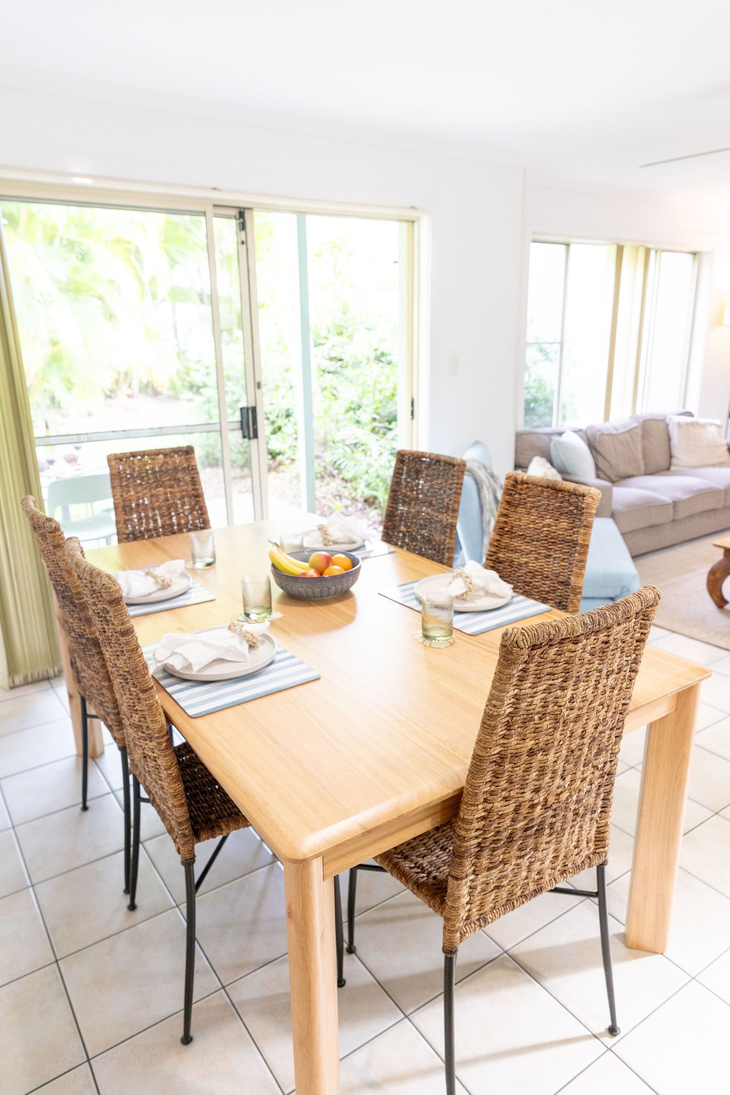 Bright dining room with woven rattan chairs and wooden table near large windows.