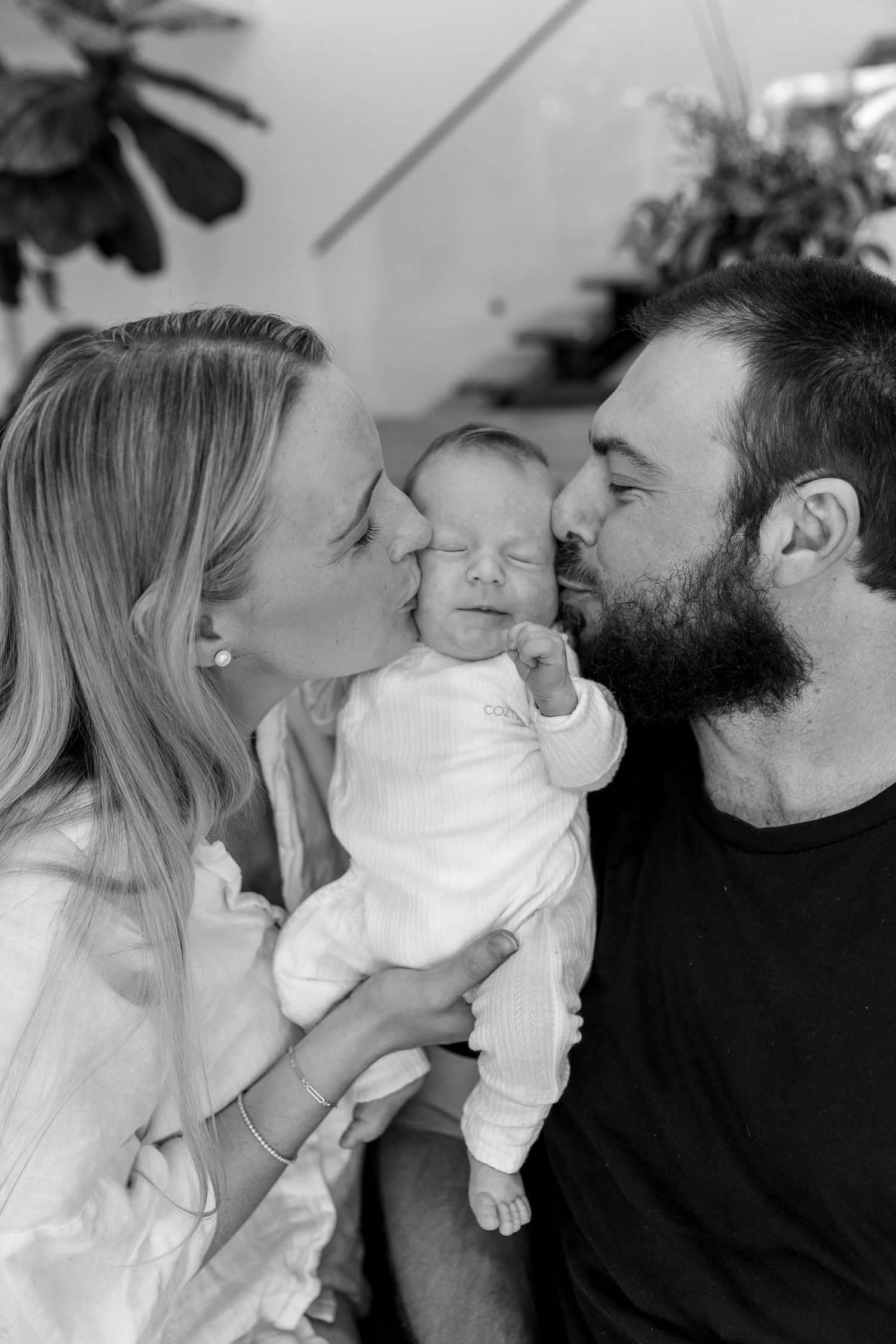 Black and white series showing parents kissing their newborn from both sides.