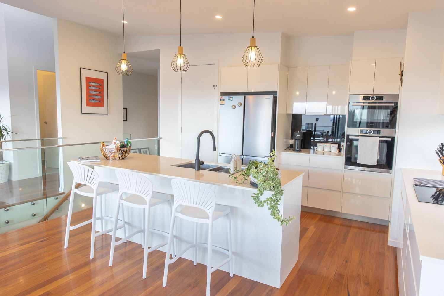 Contemporary white kitchen with pendant lighting, island seating, and stainless steel appliances.
