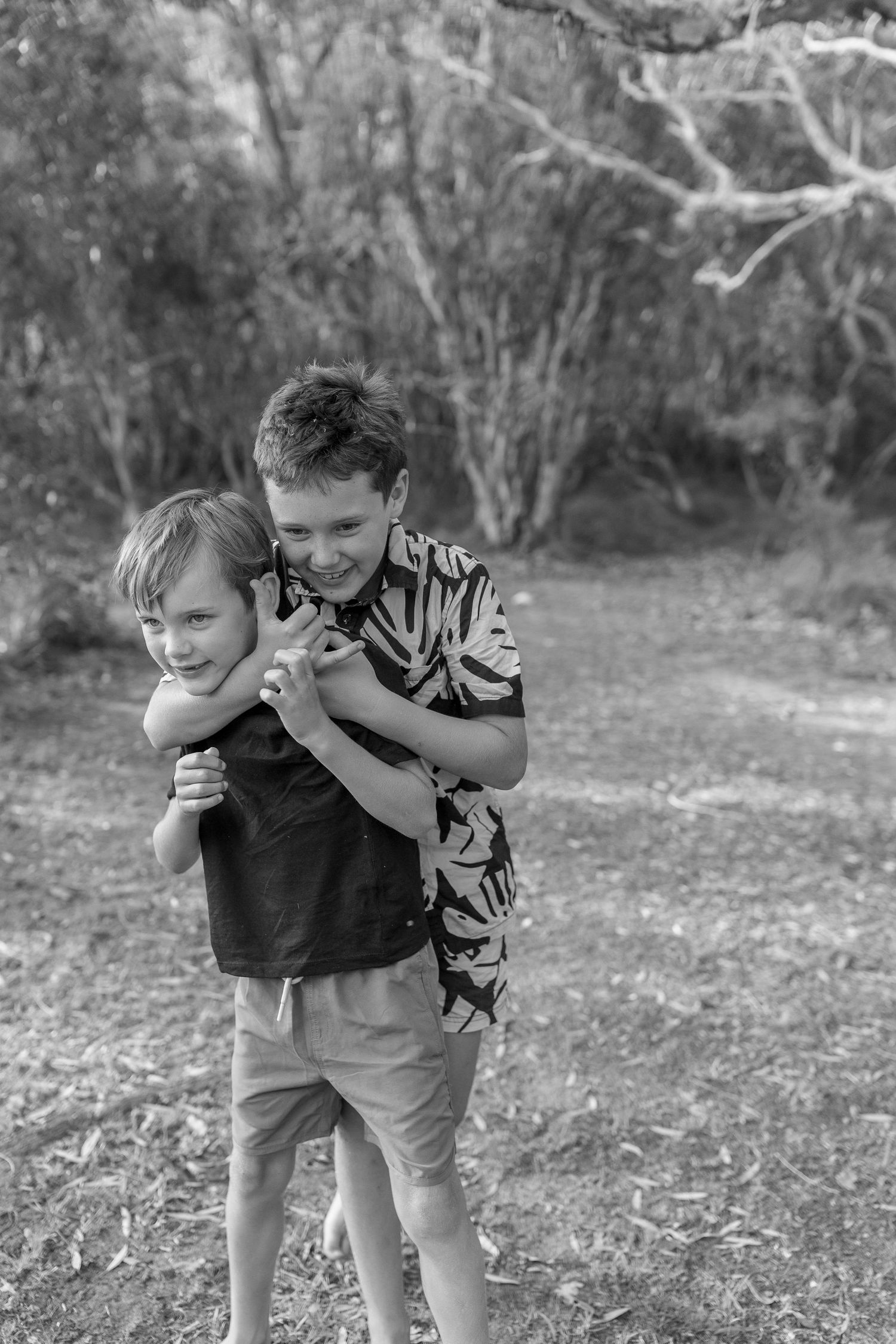 Black and white photo series of siblings playing and hugging outdoors.