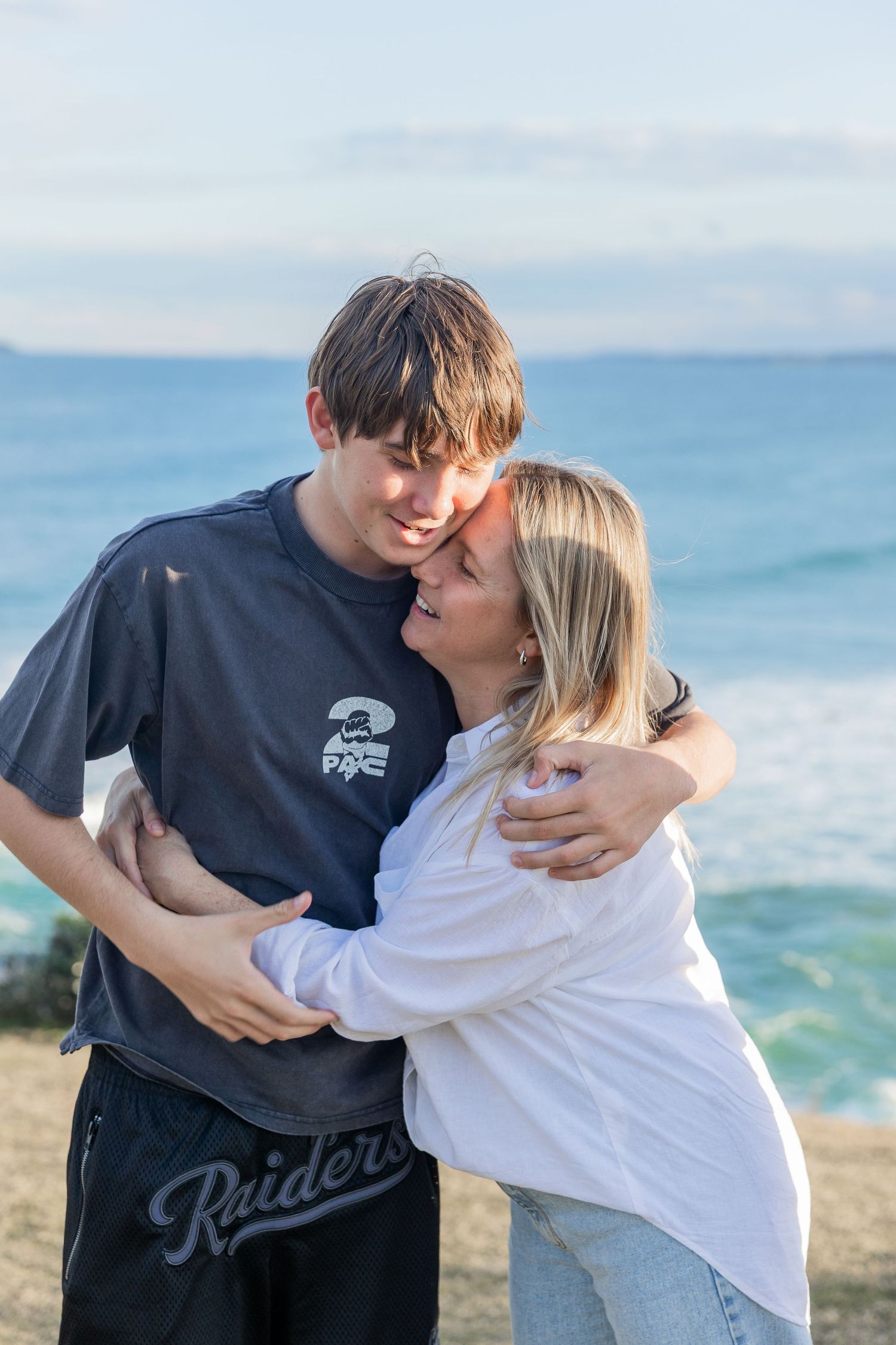 Affectionate embrace captured on a scenic coastal cliff with ocean waves behind.