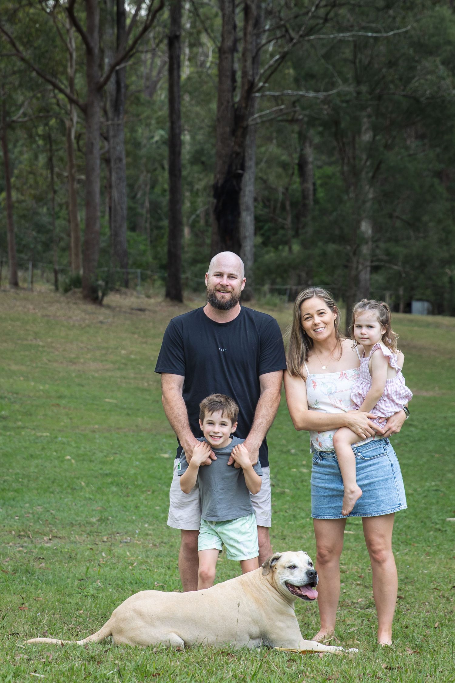 Happy family posing together with their Labrador retriever in a wooded park setting.