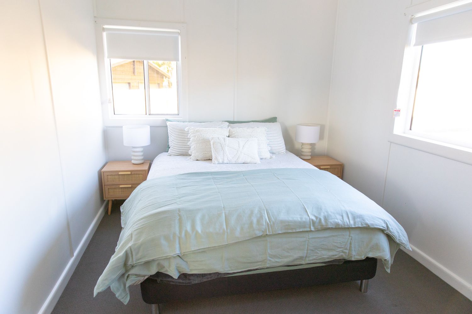 Spacious bedroom with white bedding and natural light streaming through windows.