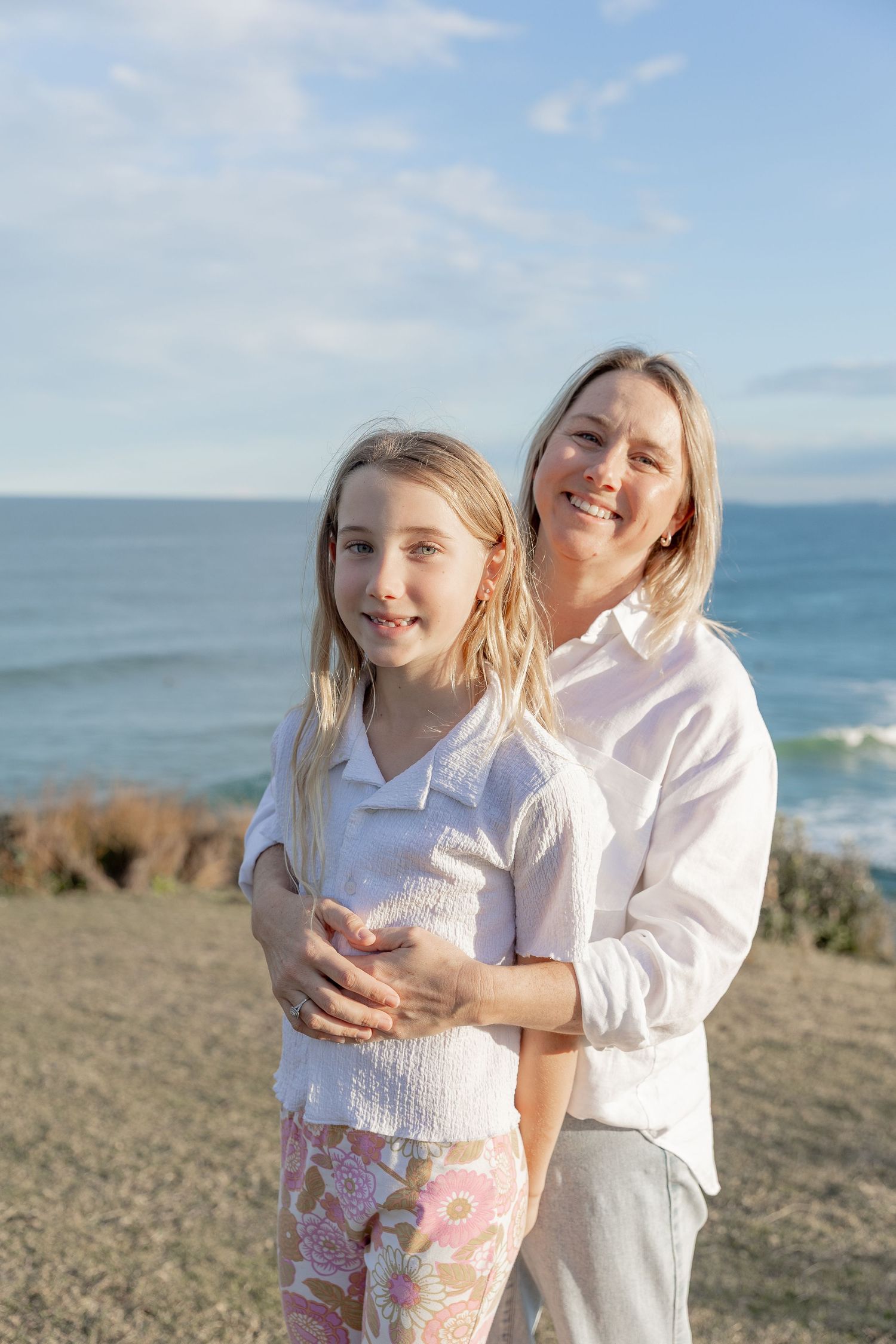 Mother and child sharing a tender moment on a coastal cliff with ocean views.