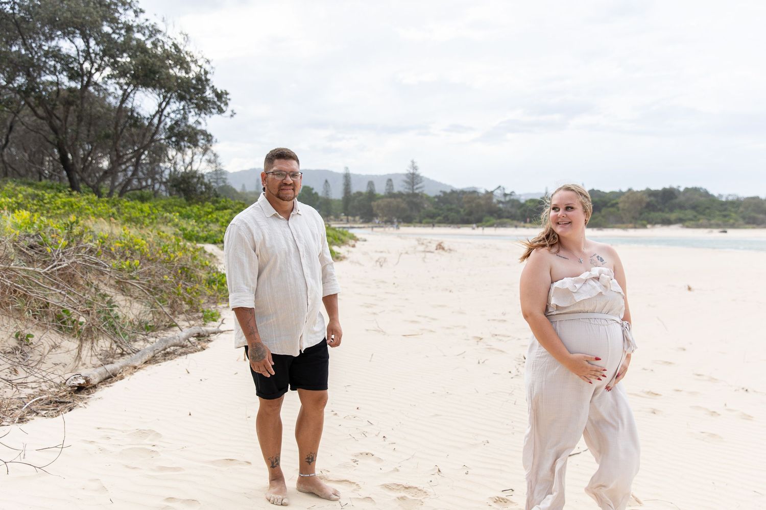 A family walks along a scenic beach shoreline in light-colored coordinating outfits.