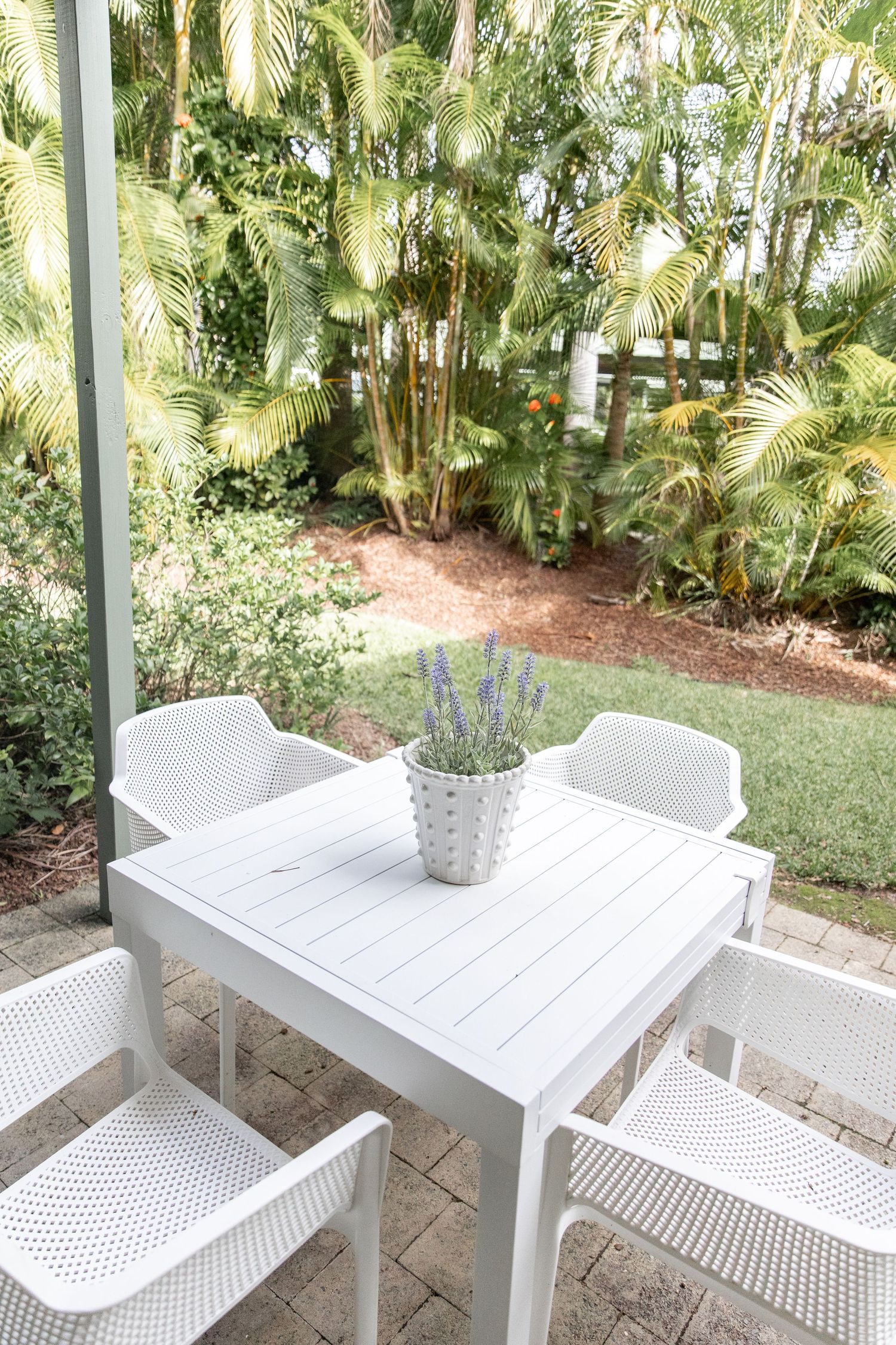 Modern white outdoor dining set with mesh chairs surrounded by lush tropical landscaping.