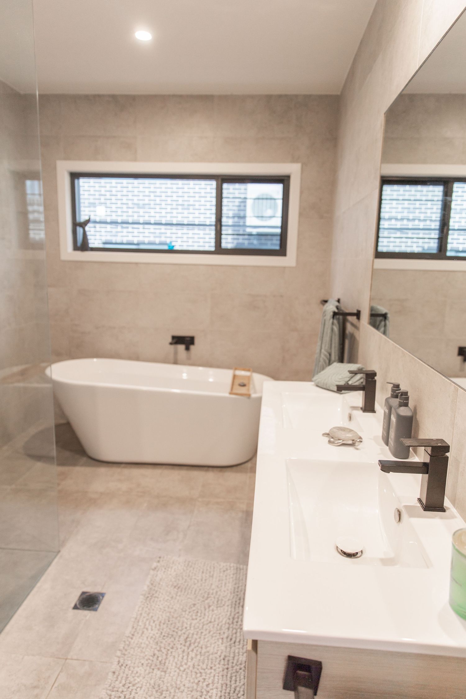 Modern bathroom featuring freestanding tub, double vanity, and large horizontal window.