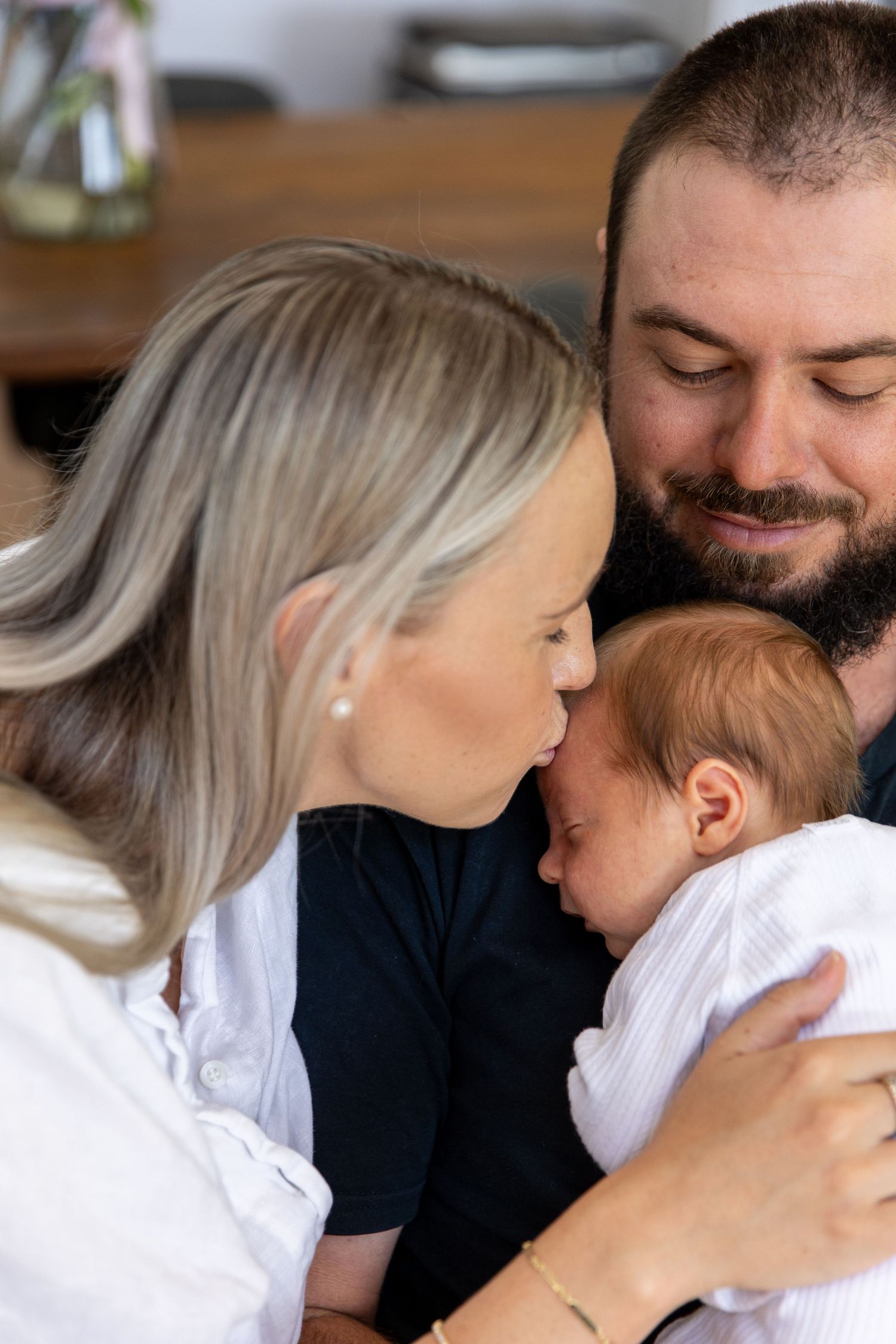 Loving parents share tender moments with their newborn baby in white clothing.