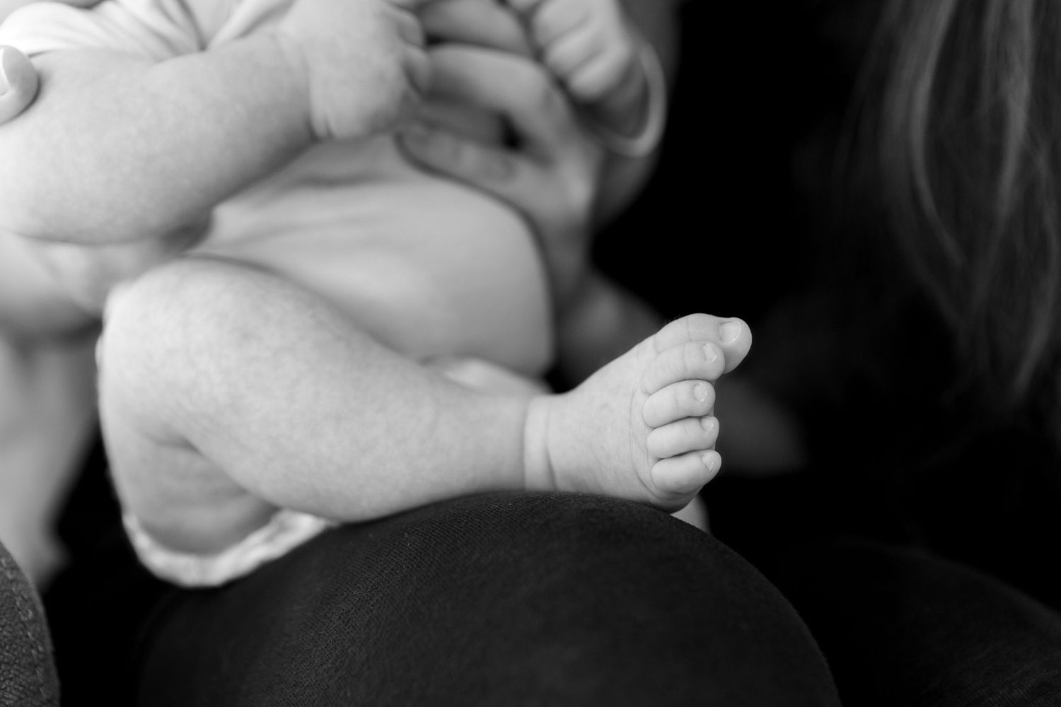 Black and white photo of a newborn baby being cradled, showcasing tiny chubby feet and legs in mother's arms.