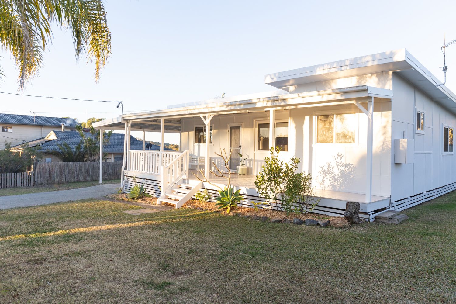 Panoramic view of a white residential property with palm trees and landscaped yard.