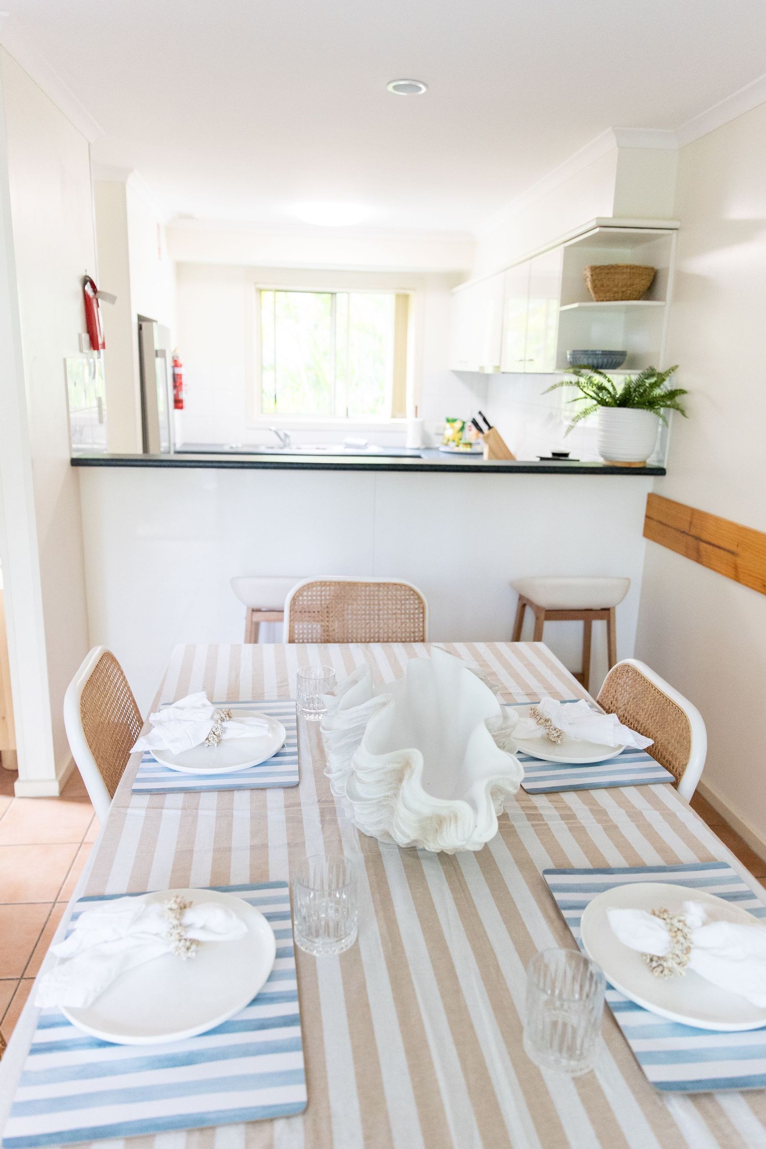 Elegant dining setup with striped tablecloth and white place settings in modern beach house.