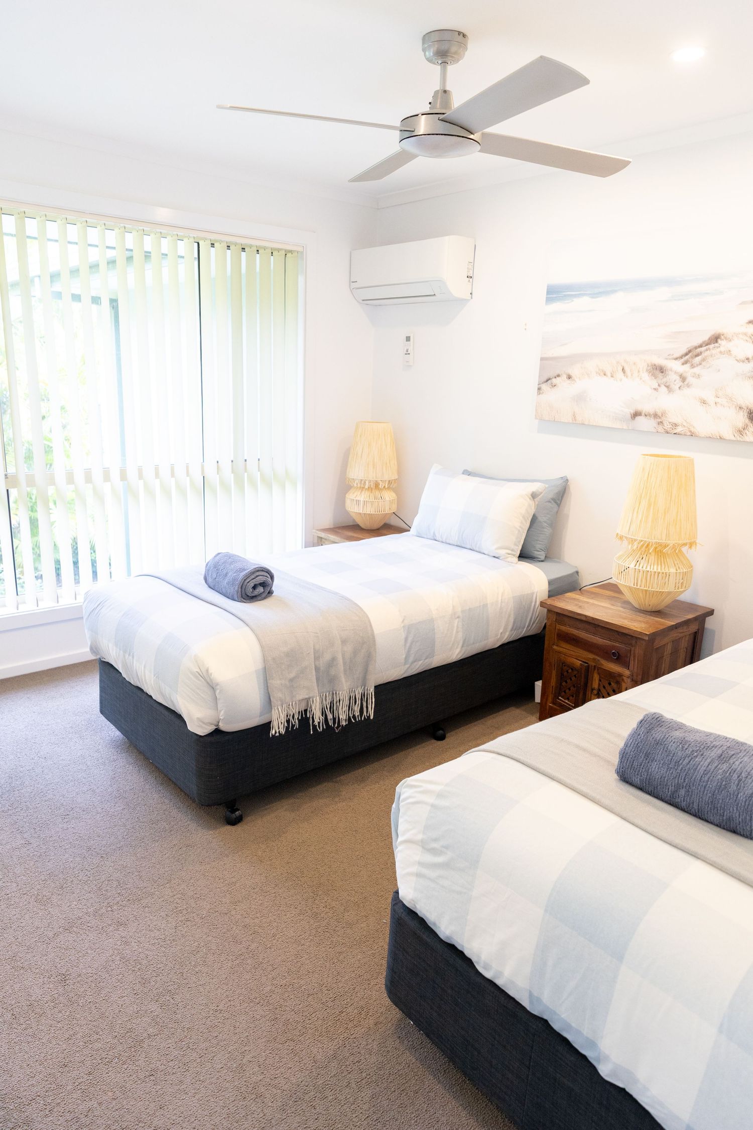 Bright bedroom with white bedding, ceiling fan, and coastal artwork on the walls.