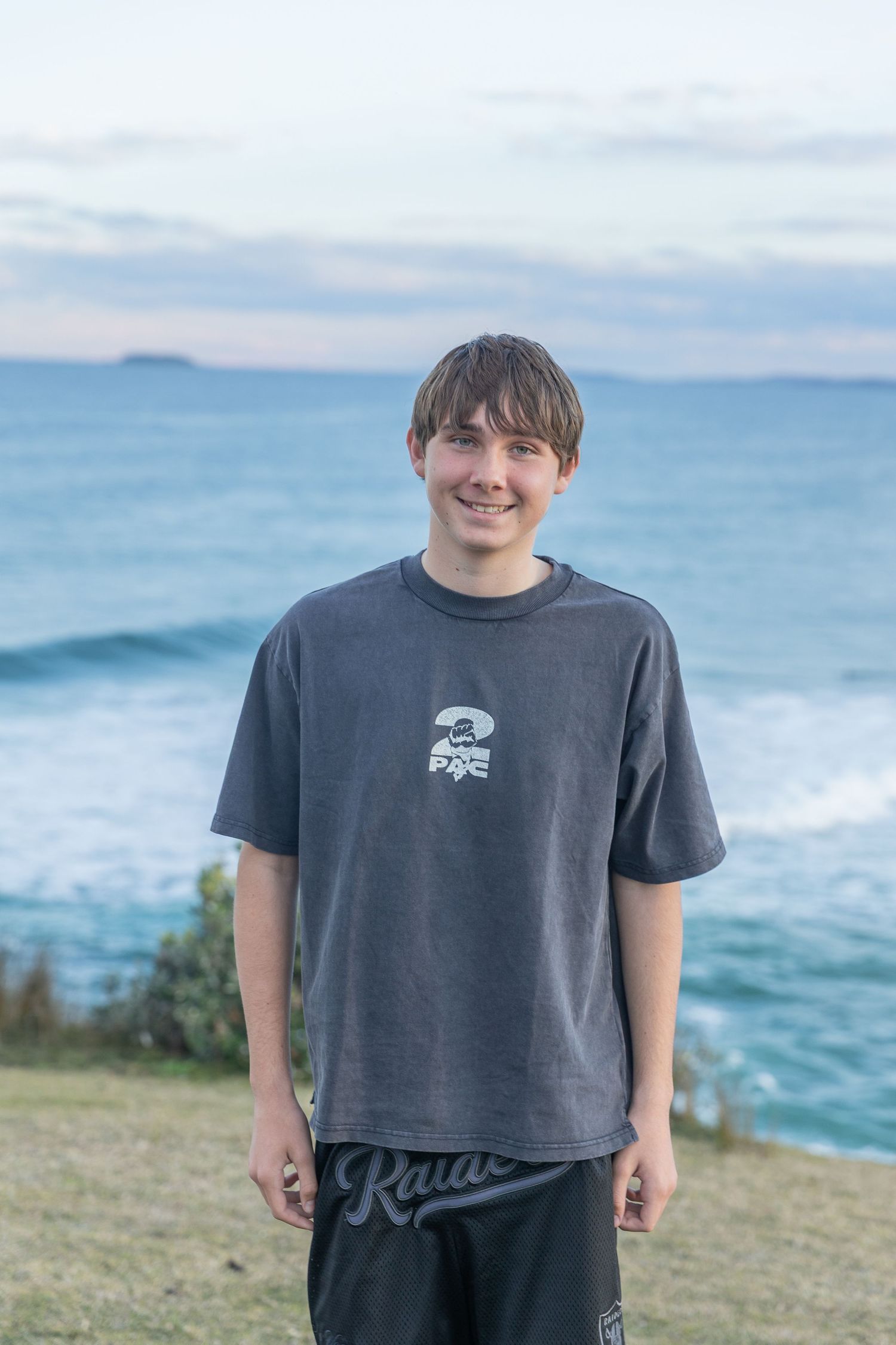Person in dark t-shirt standing on grassy cliff with ocean waves behind.