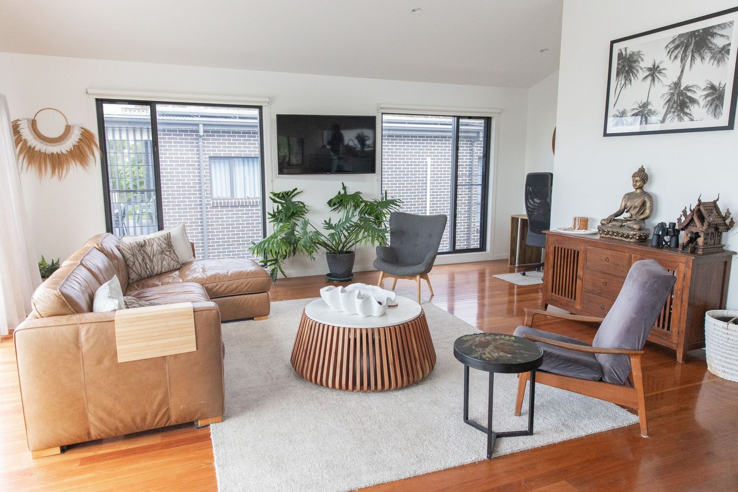 Modern coastal living room with tan sectional sofa, round wooden coffee table, and tropical palm wall art.