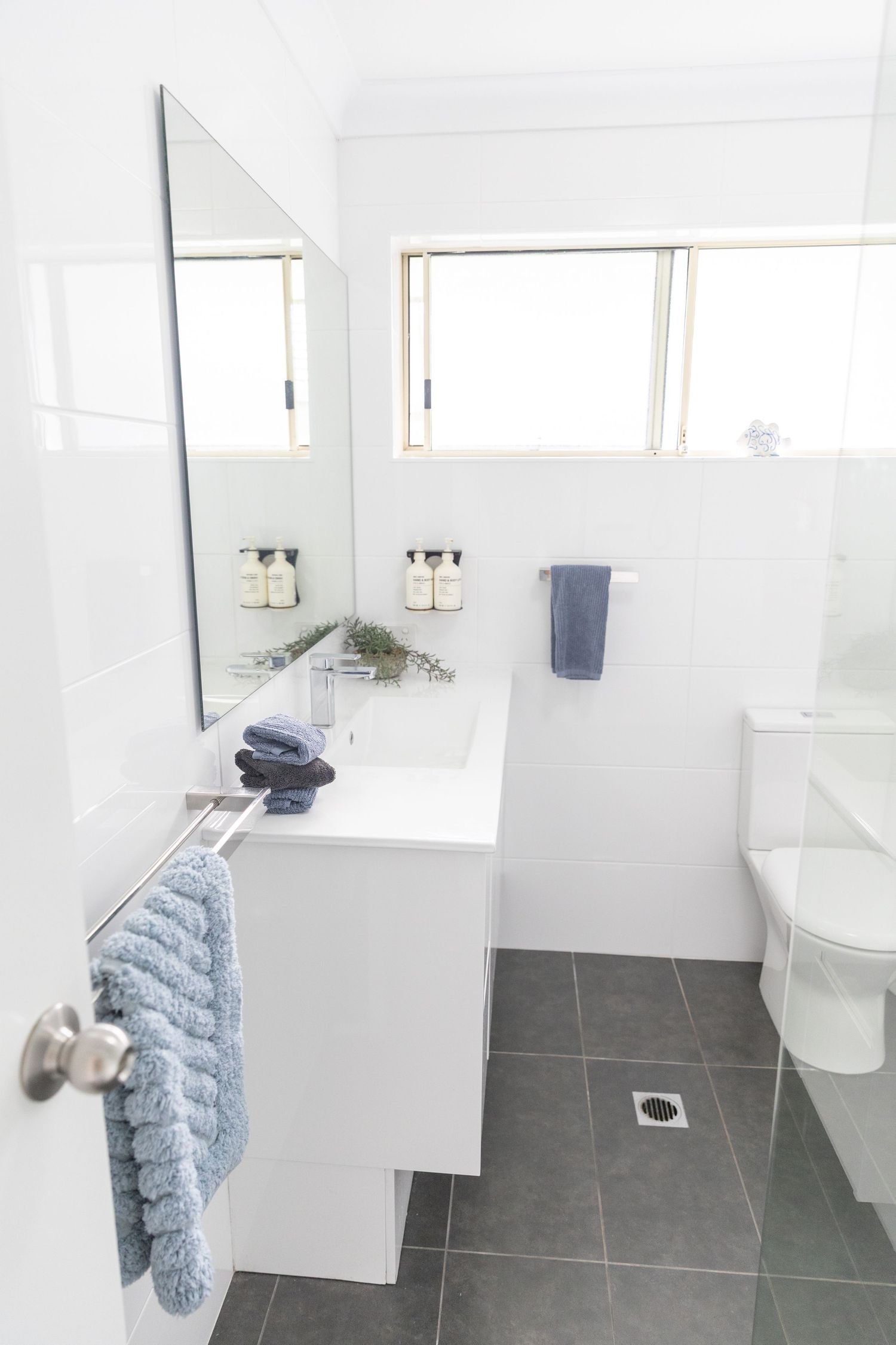 Modern white bathroom with grey floor tiles and blue towel accents.