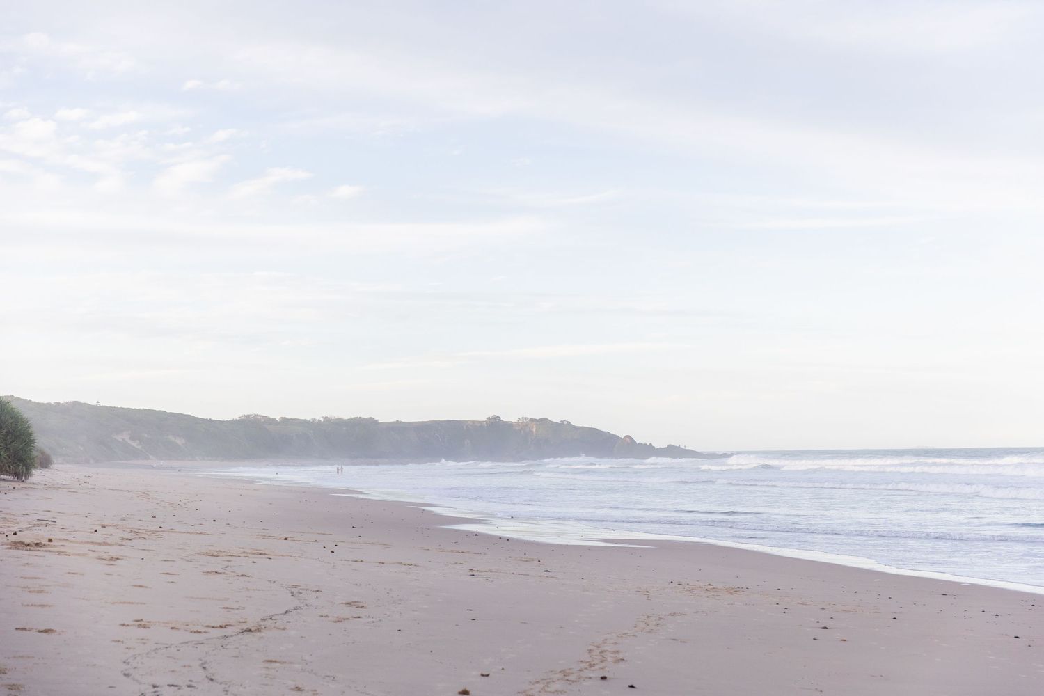 Panoramic view of a serene beach coastline with gentle waves and cloudy sky.