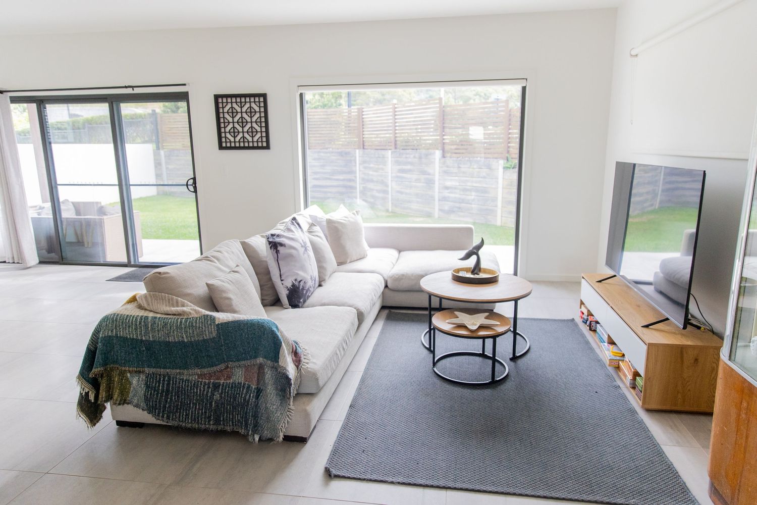Contemporary living room with L-shaped sectional, round nesting tables, and wooden TV unit.