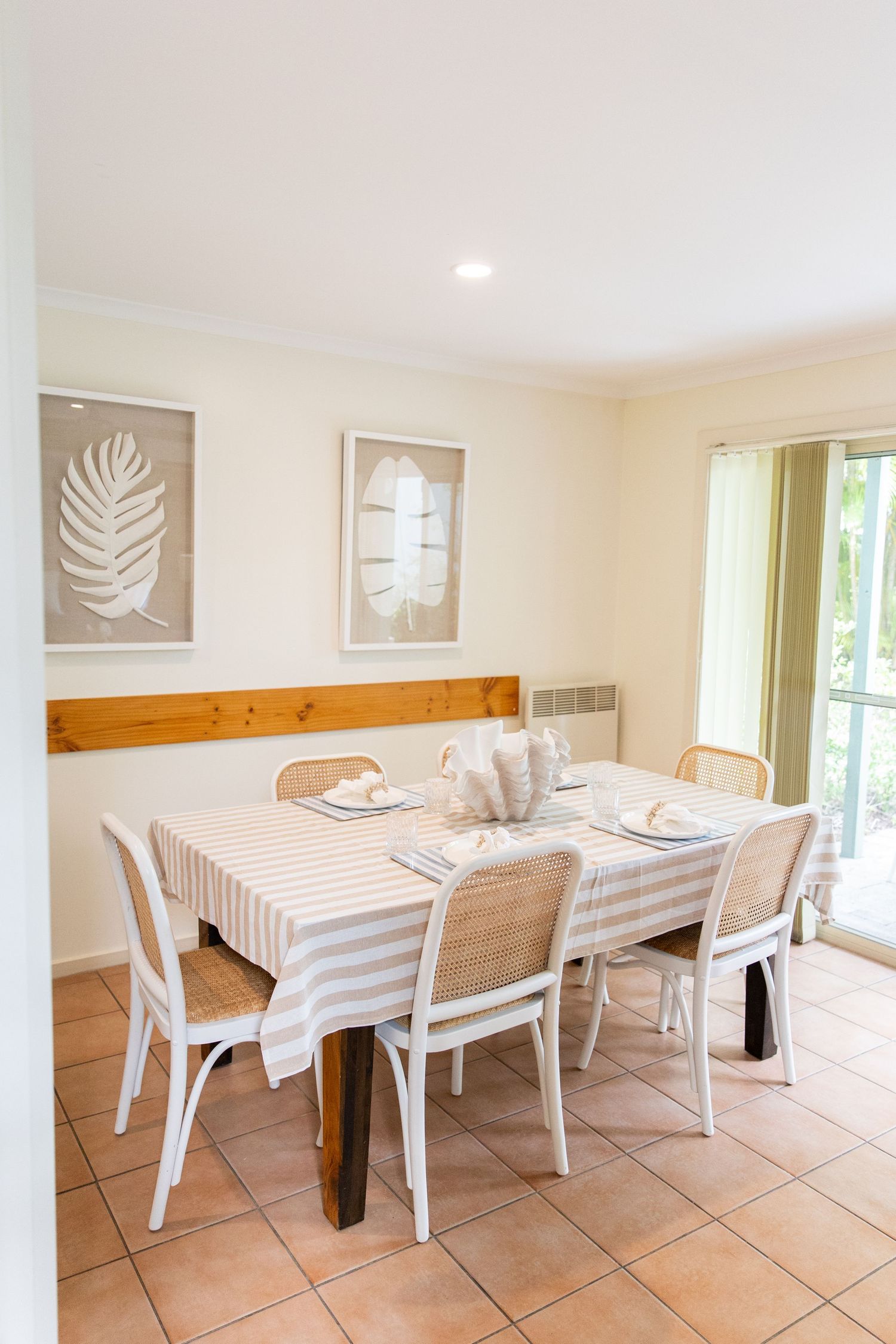 Bright dining area with white chairs, wooden table, and palm leaf artwork on walls.