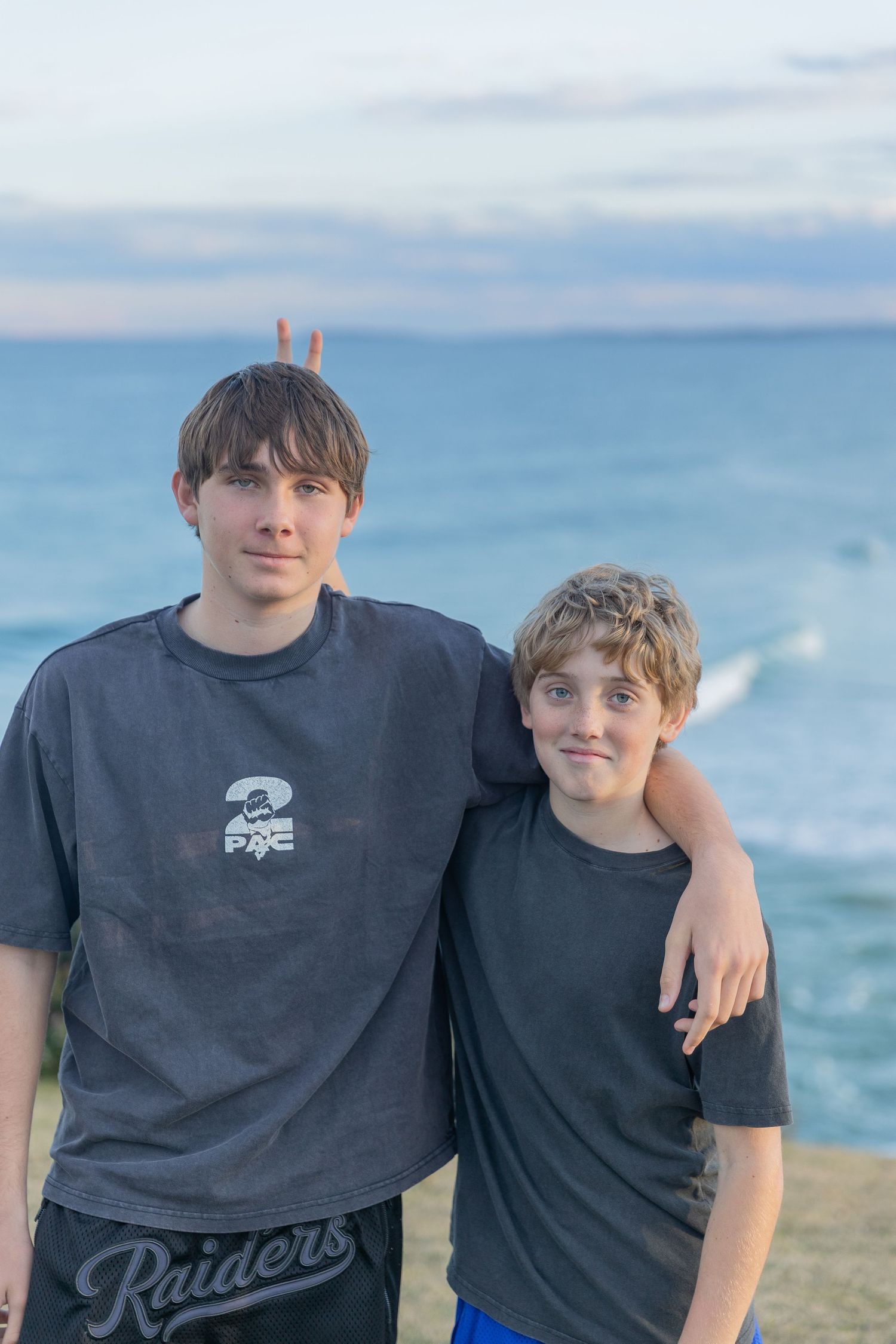 Two young people posing together on a coastal cliff with ocean waves in background.