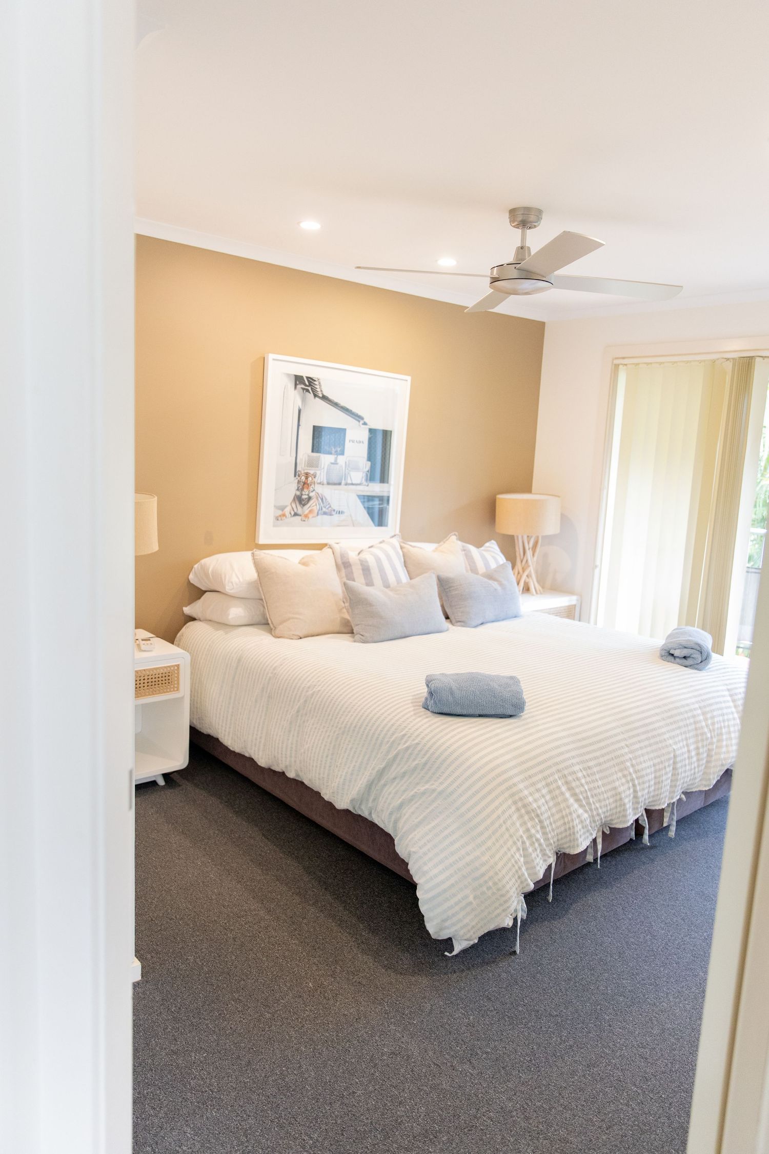 Modern bedroom with white bedding, ceiling fan and bright natural lighting.