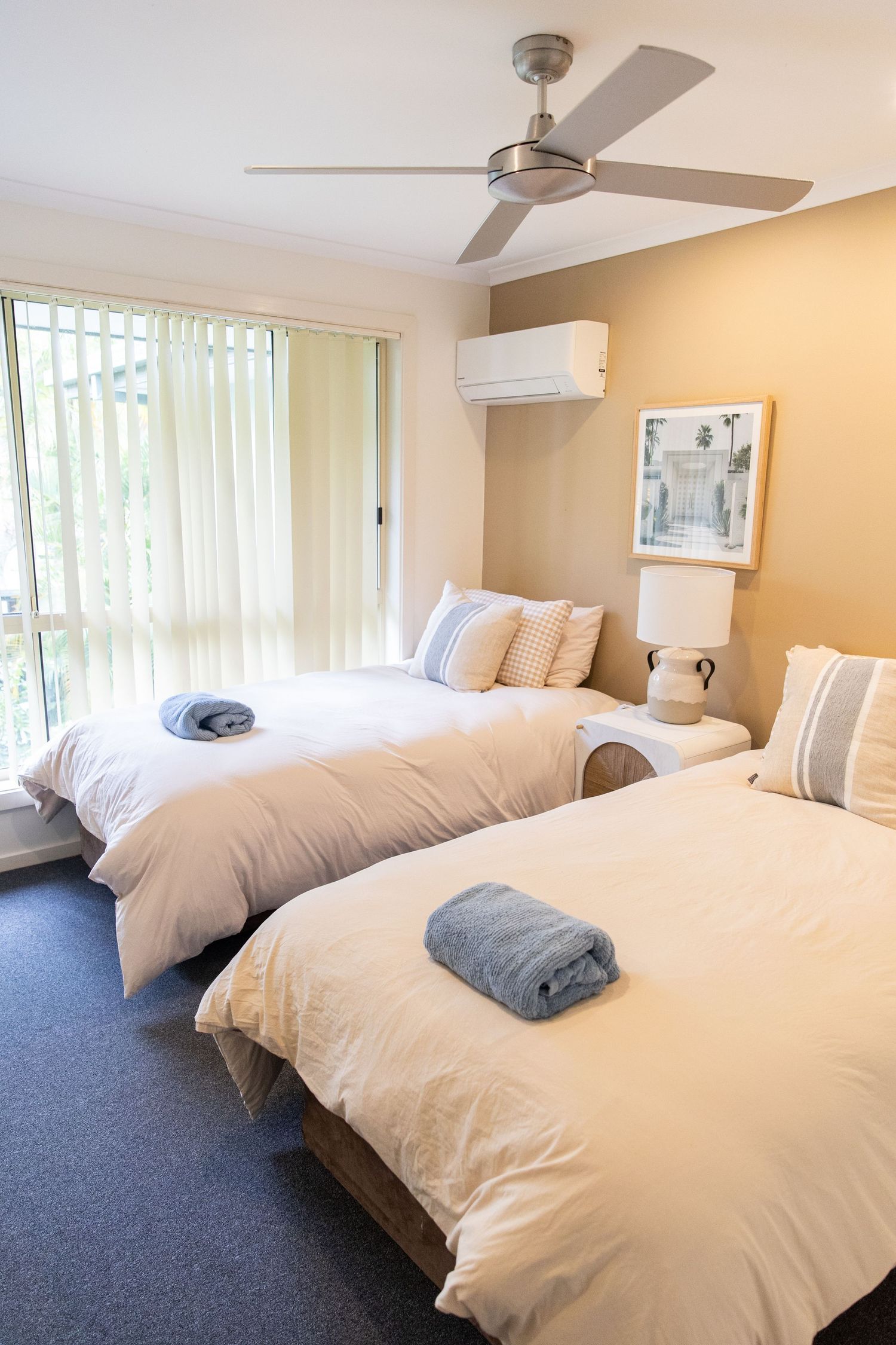 Spacious bedroom with white bedding, ceiling fan, and carpeted flooring in neutral tones.