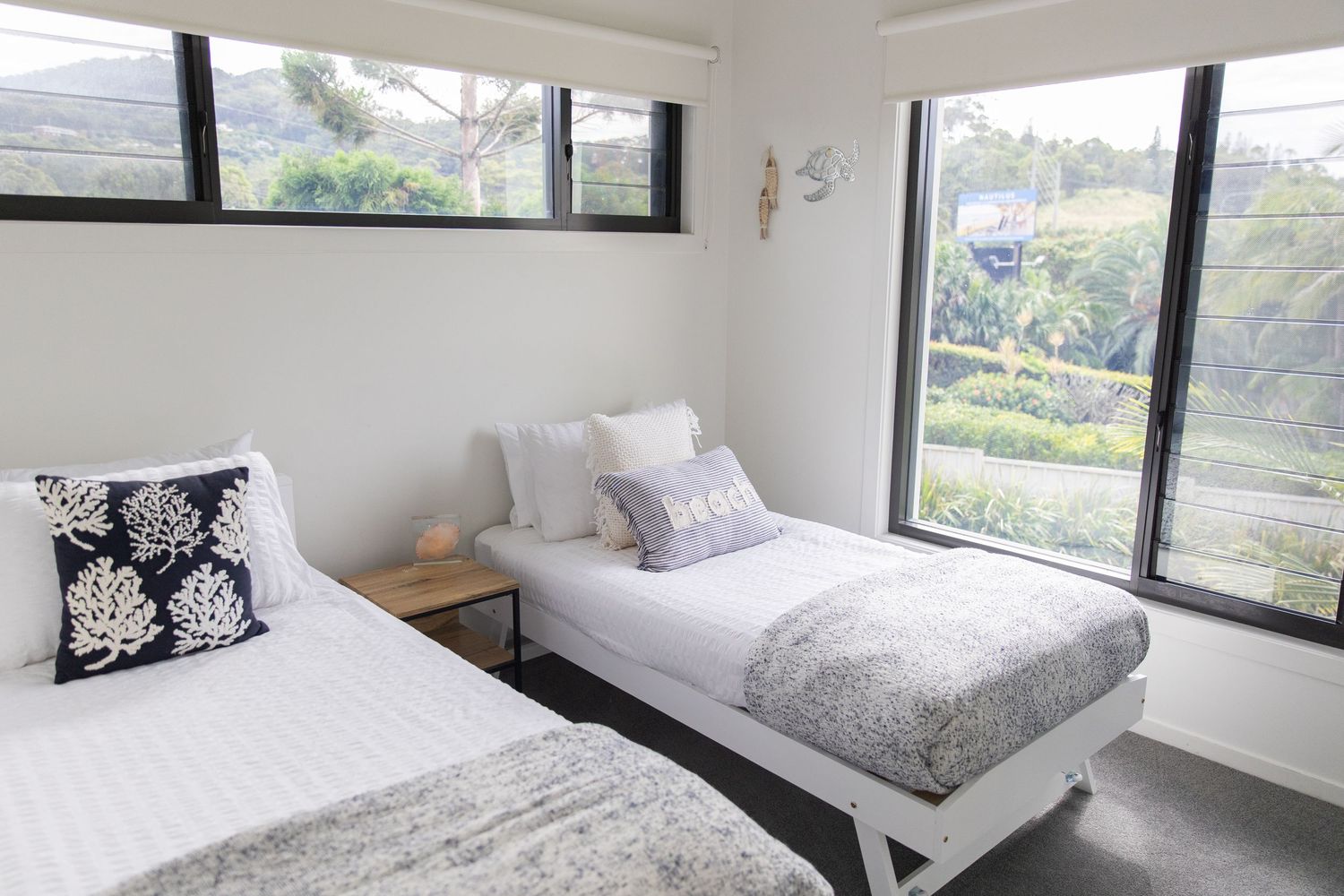 Bright guest bedroom with twin beds, large windows, and black and white decorative pillows.
