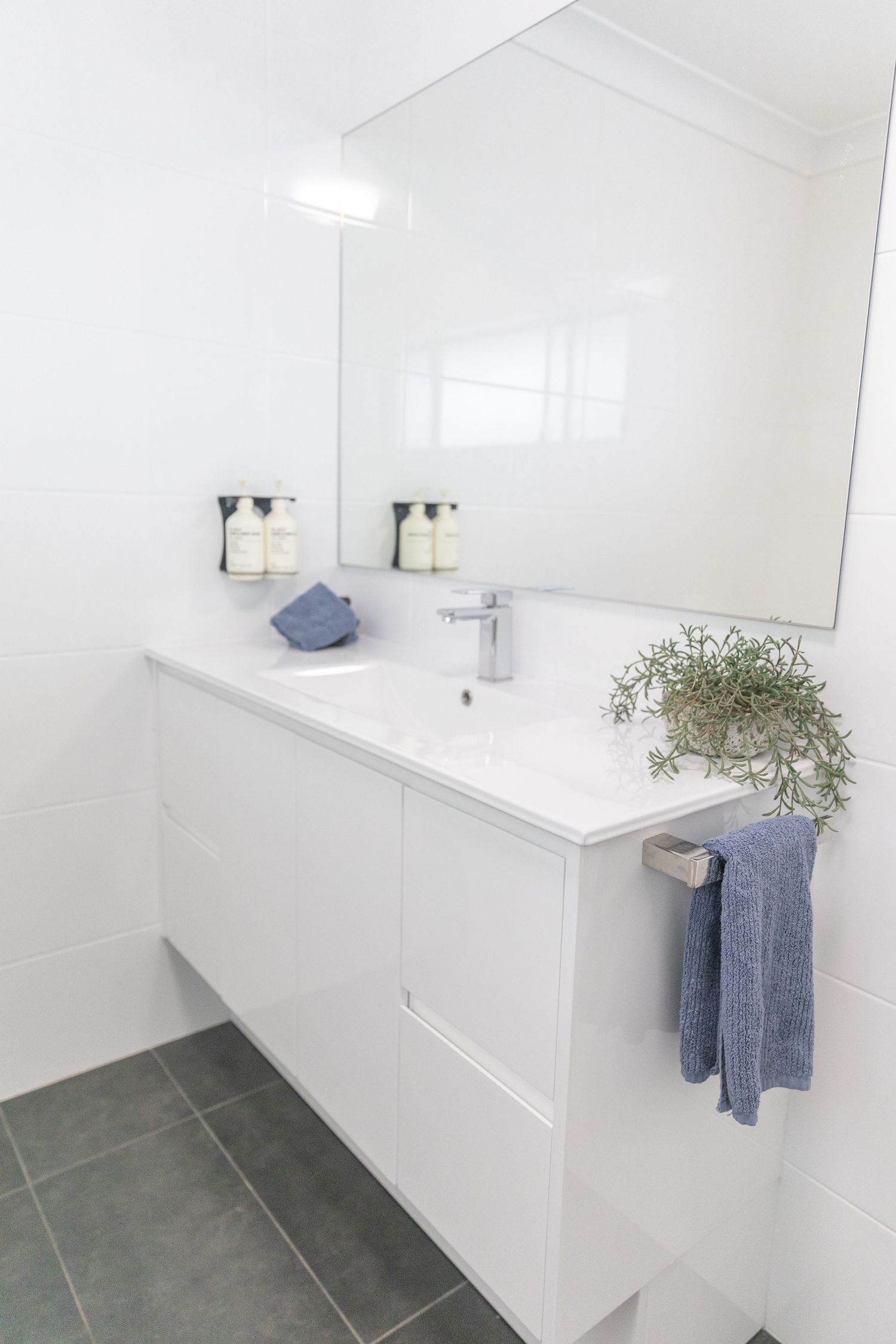Minimalist bathroom featuring white walls, grey floor tiles and blue towel accessories.