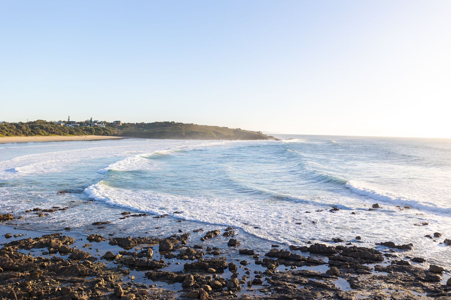Scenic coastal beach view with rocky shoreline and rolling waves.