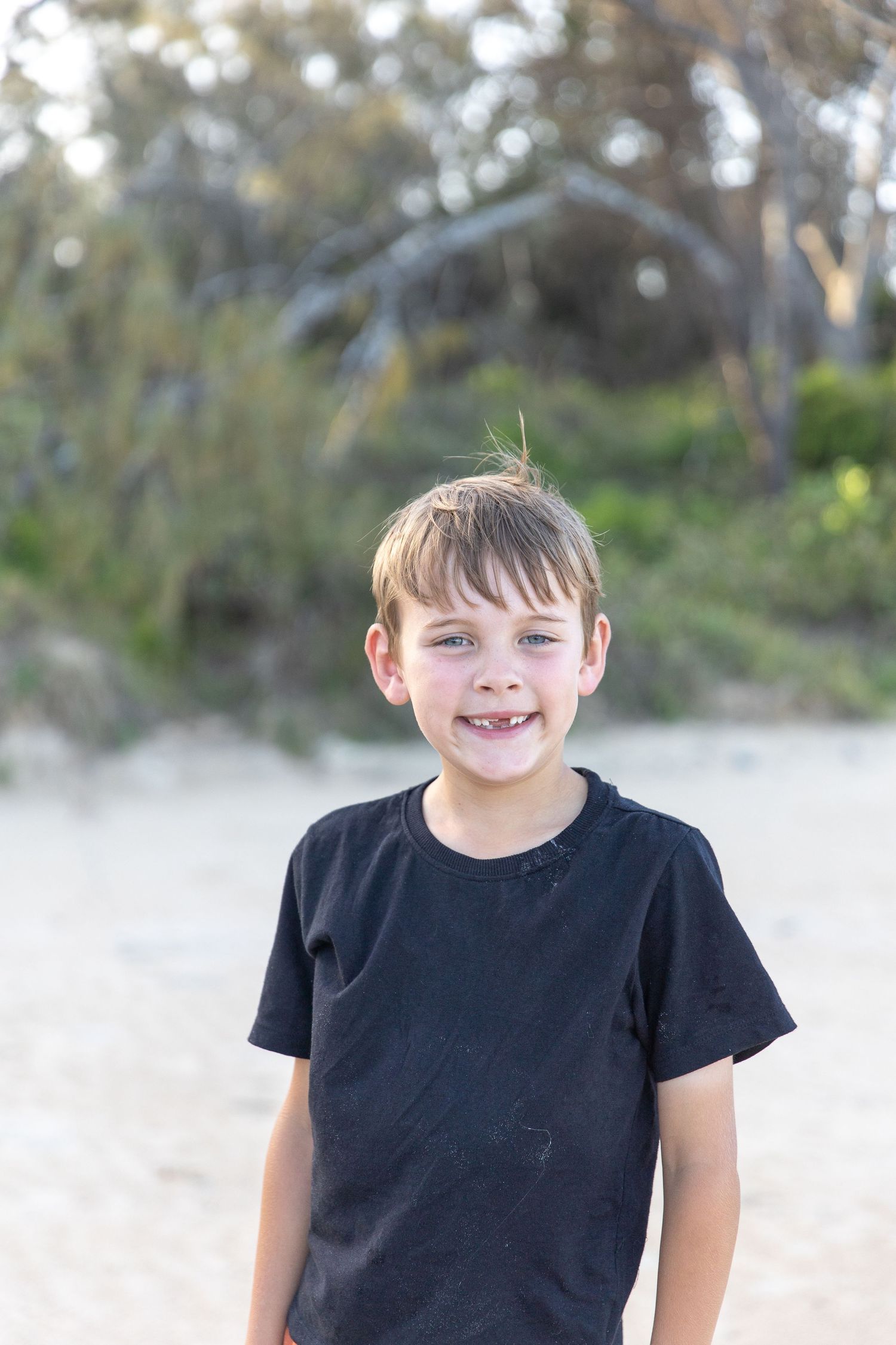 Child in black t-shirt smiling against a blurred natural background.