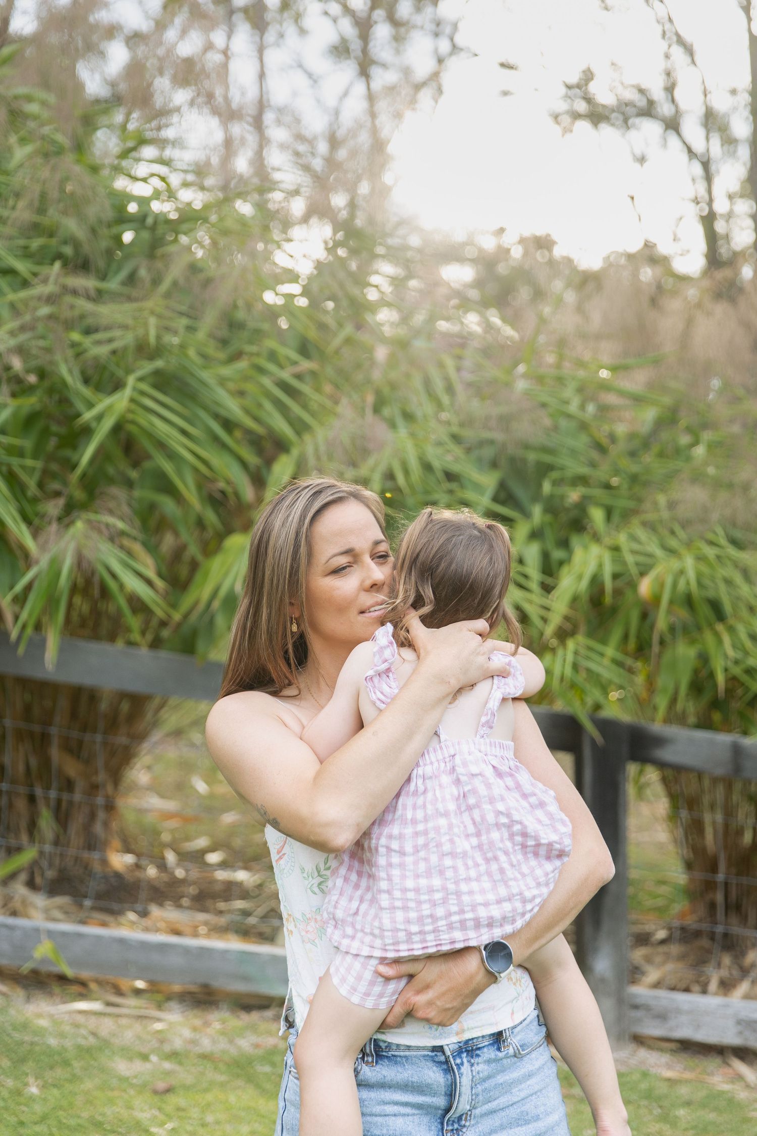 A mum & her daughter in a garden setting with bamboo plants and natural sunlight filtering through the background.