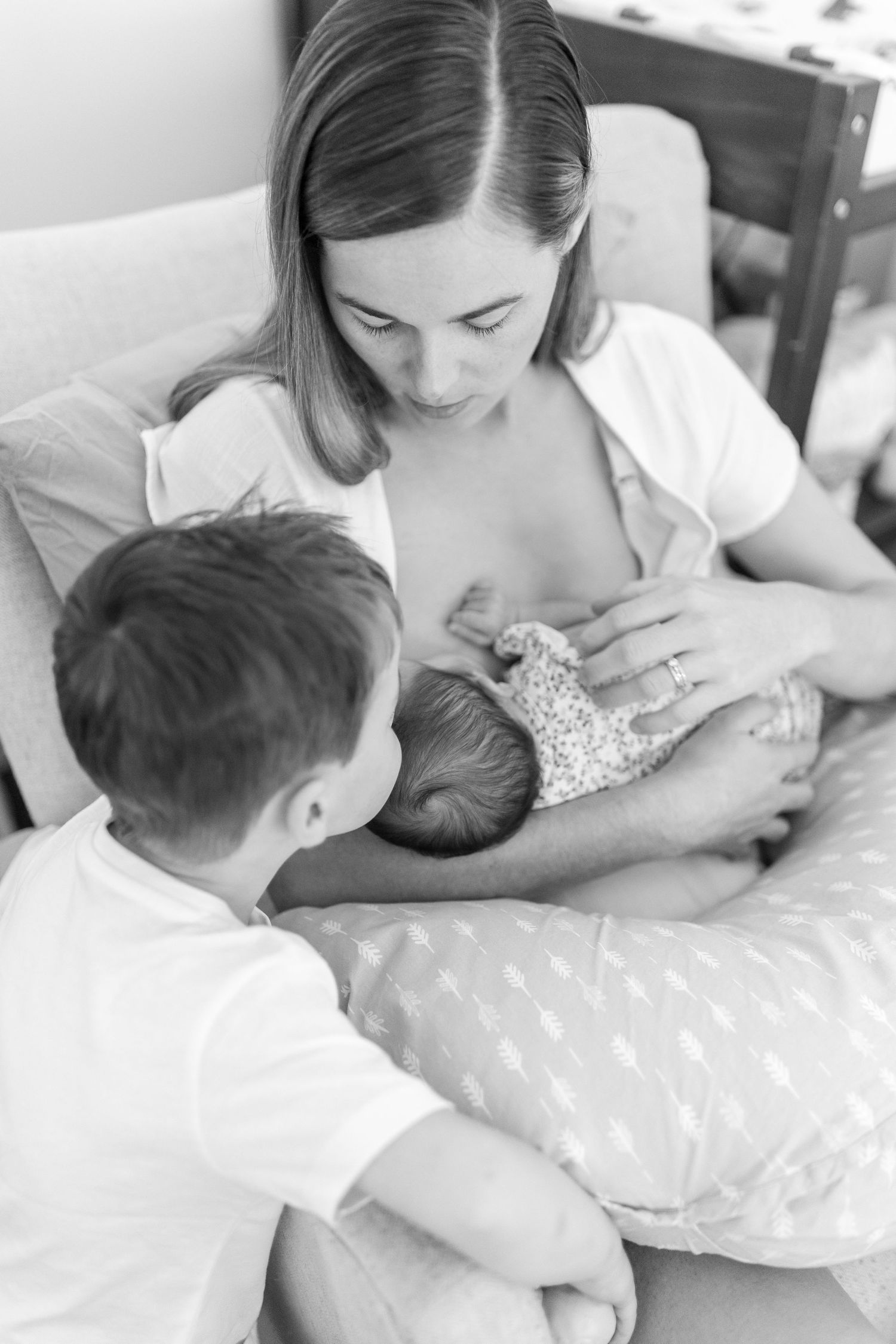 Black and white photo of a mother breastfeeding her newborn while an older child sits beside her. Coffs Coast photographer.