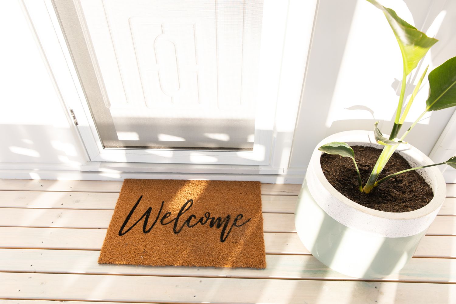 Welcome mat and potted plants decorating a bright white entryway.