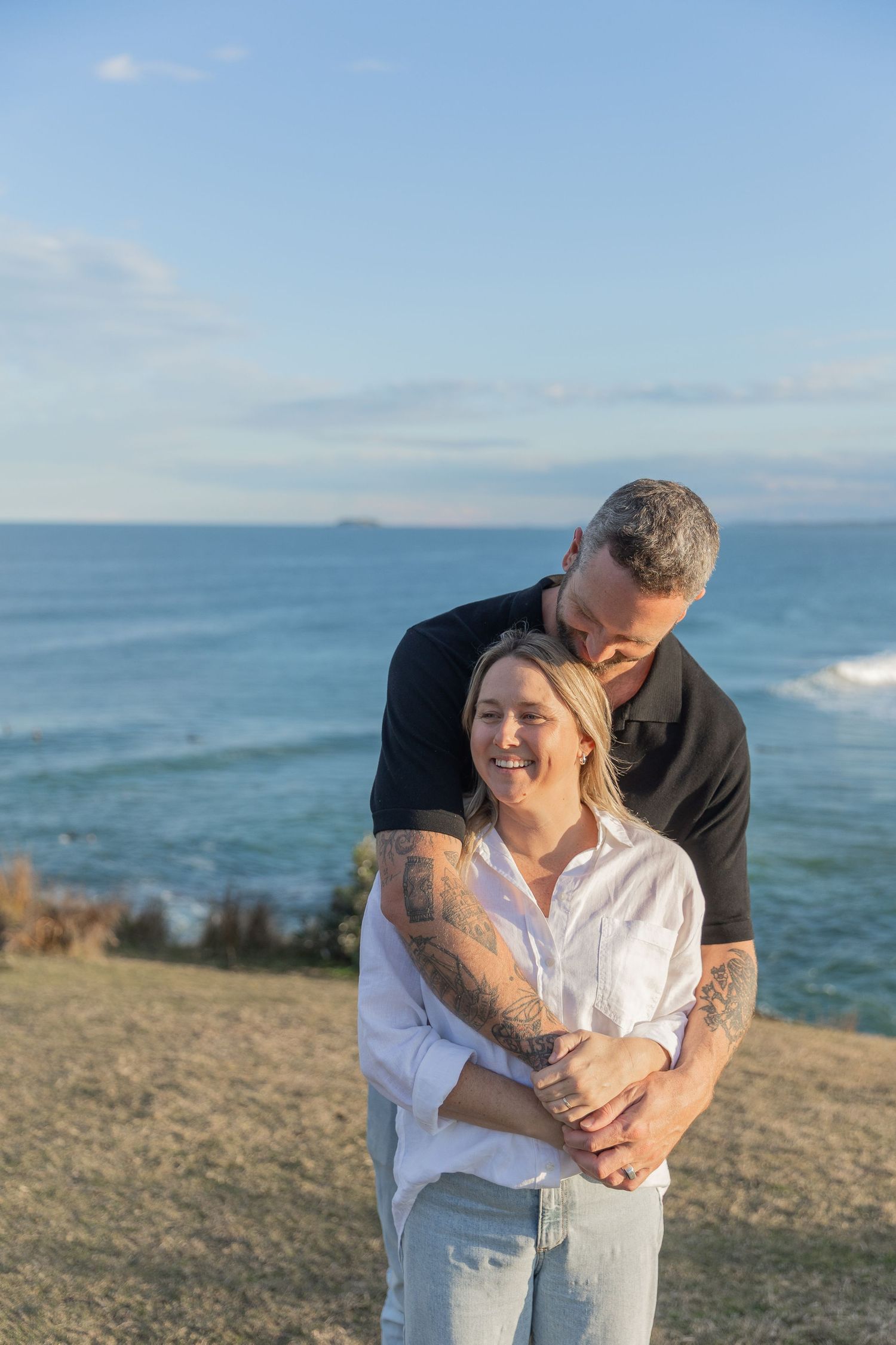 Couple sharing an intimate moment on a clifftop with ocean views at sunset.