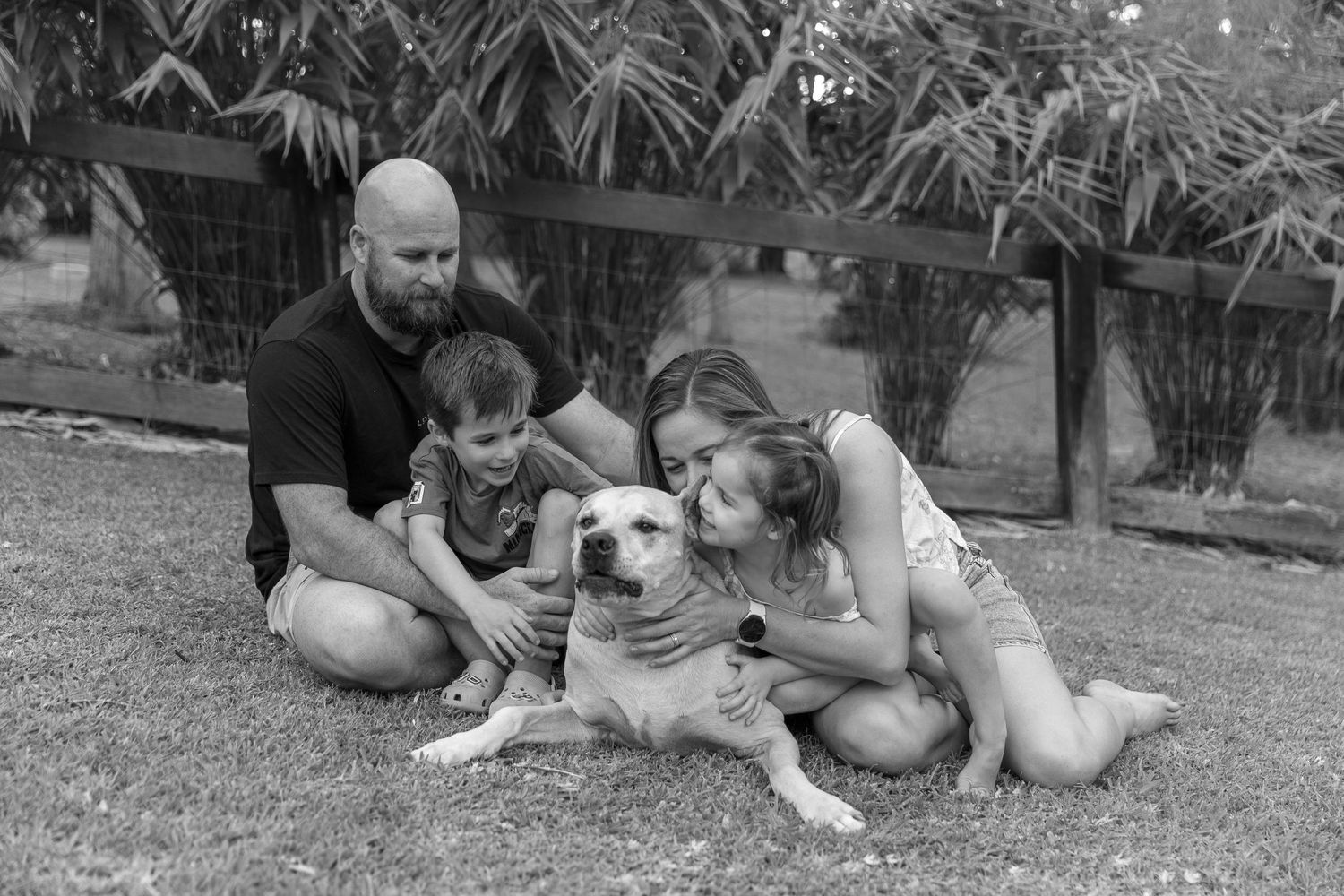 Family and pet dog relaxing together on grass under palm trees.