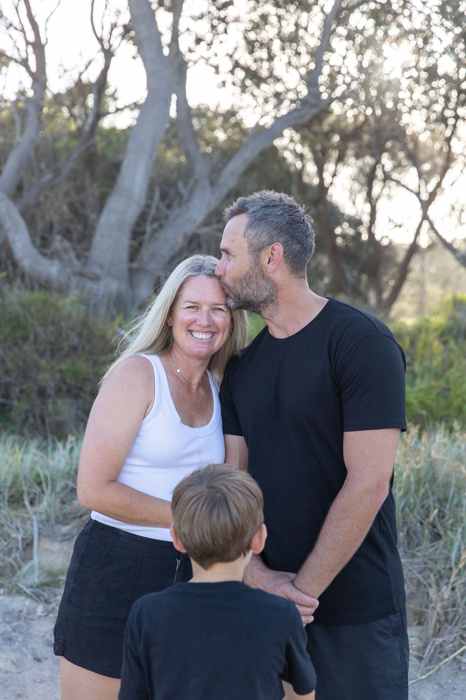 Family sharing affectionate moments against a backdrop of trees at sunset.