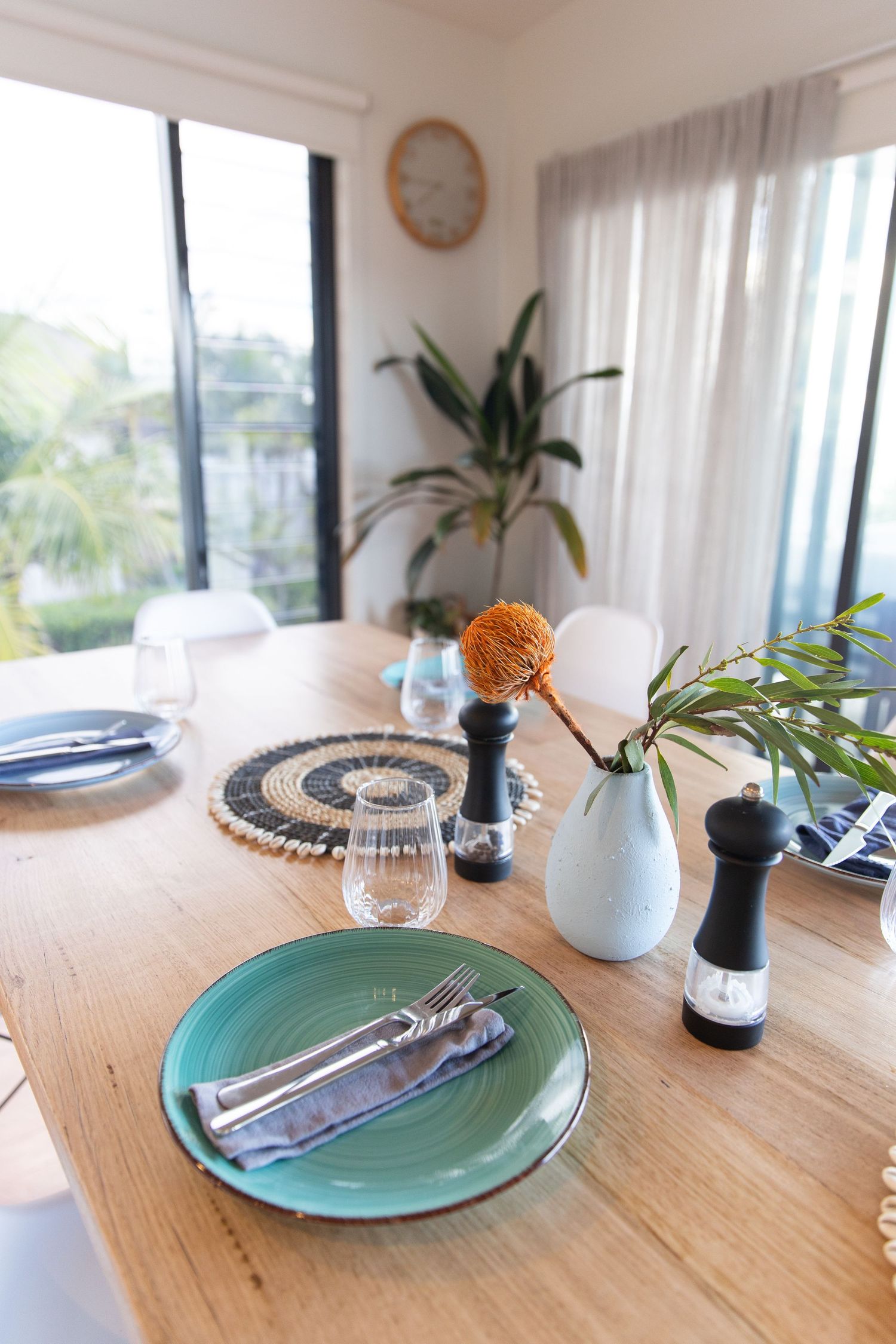 Dining table setting with turquoise plates, woven placemats, and white ceramic vases.