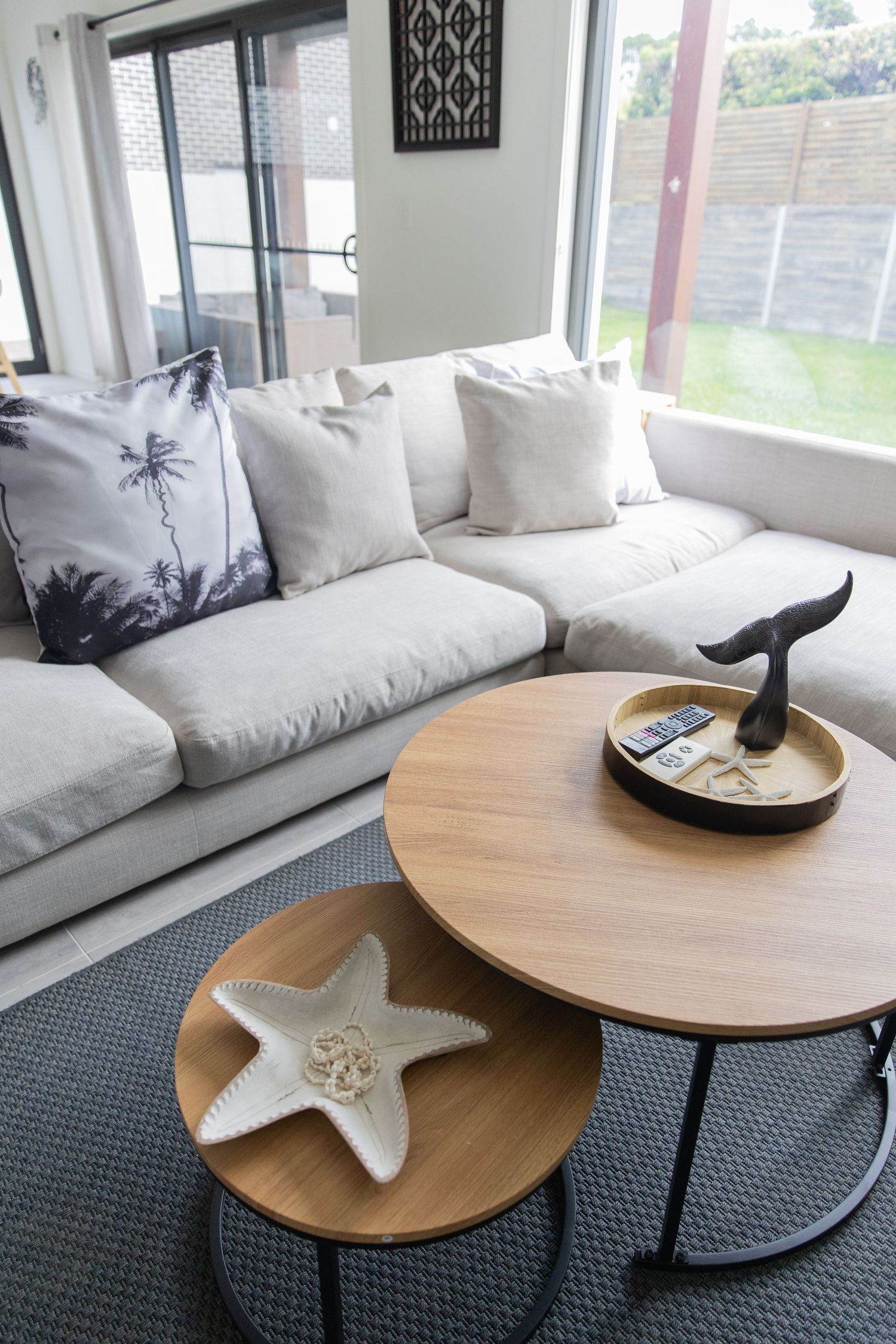 Coastal-themed living area with white sofa, nested wooden coffee tables, and starfish decor.