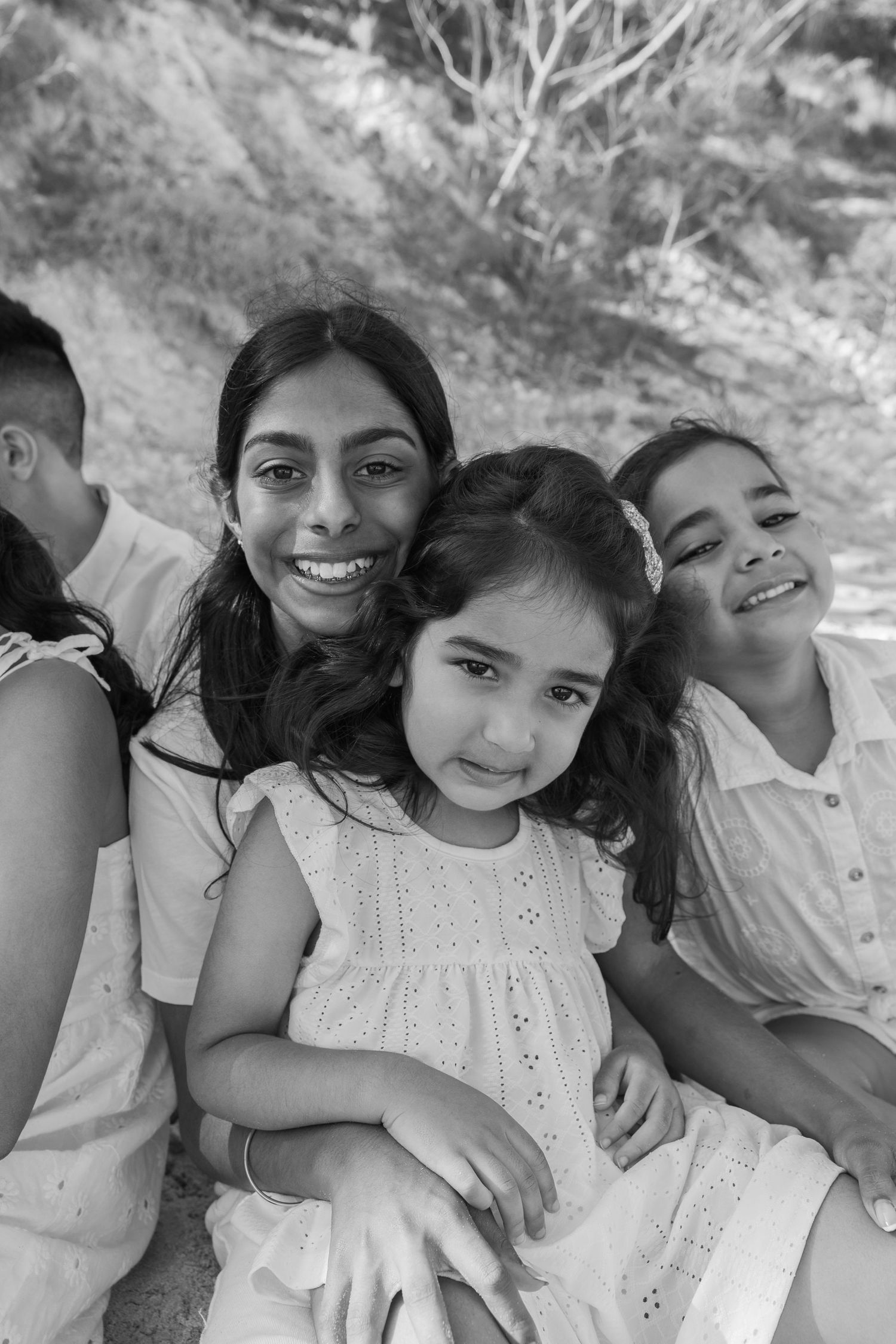 Black and white photo of a smiling mother with three children sitting together outdoors in a loving family portrait.