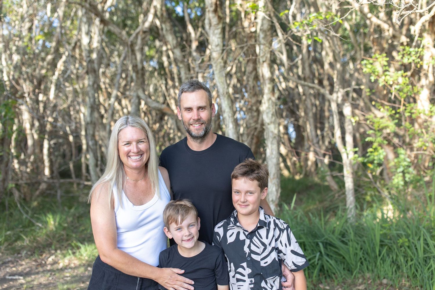 A family plays and hugs together in a wooded outdoor setting.