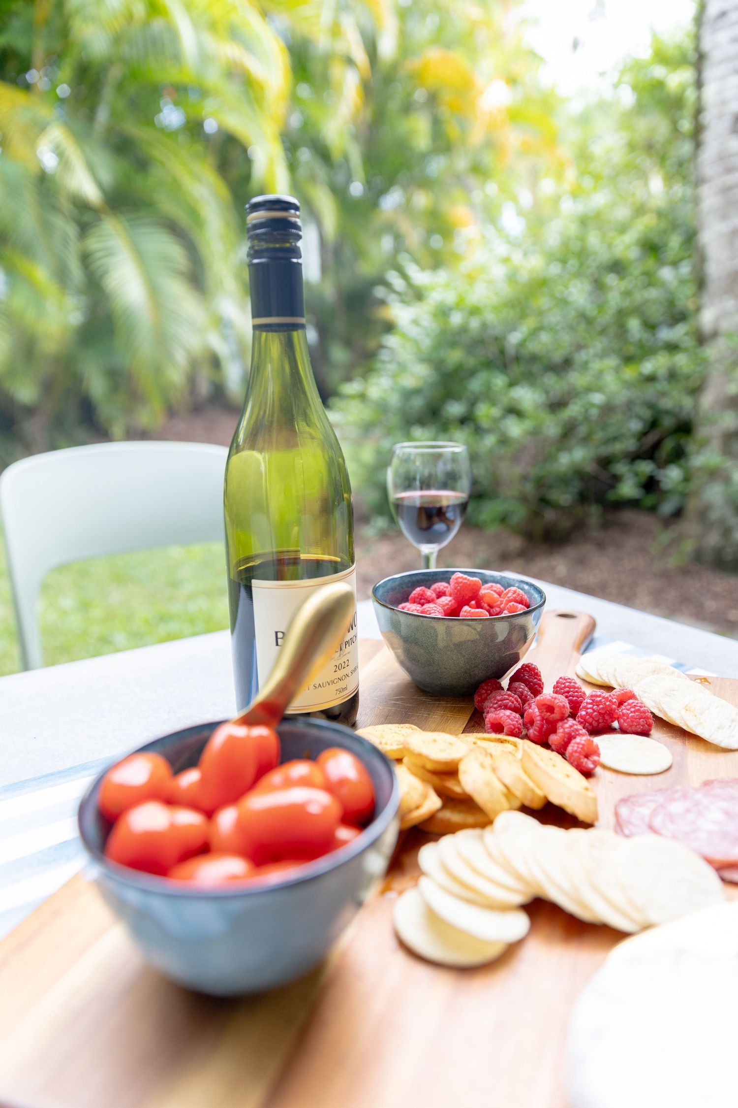 Fresh appetizer spread with wine, tomatoes, and raspberries on outdoor table.