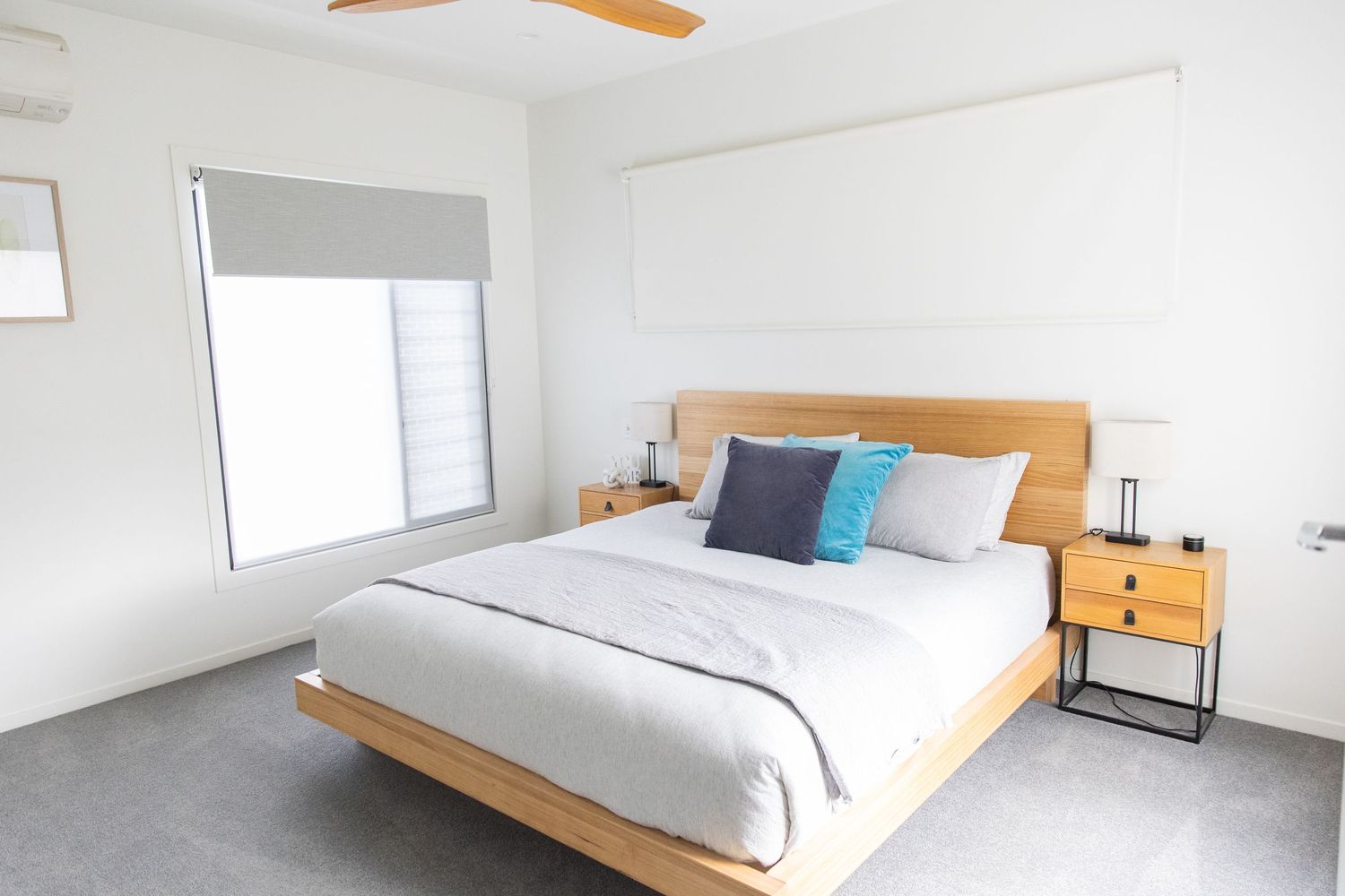 Minimalist bedroom interior with wooden bed frame and white walls.