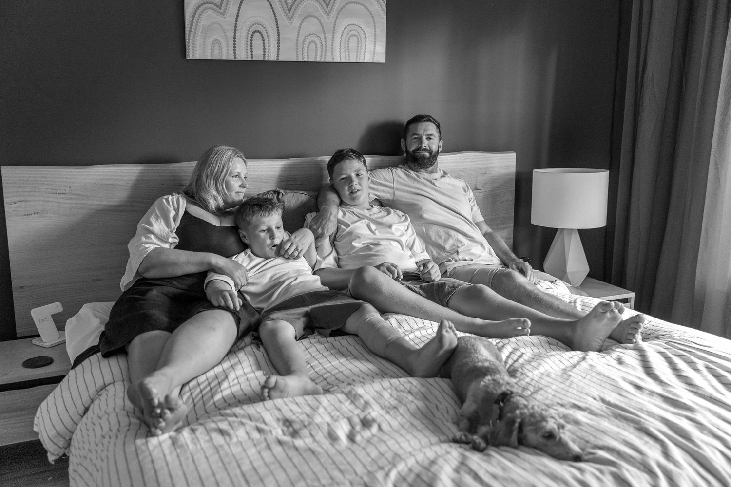 Black and white image of family members relaxing together on a bed.