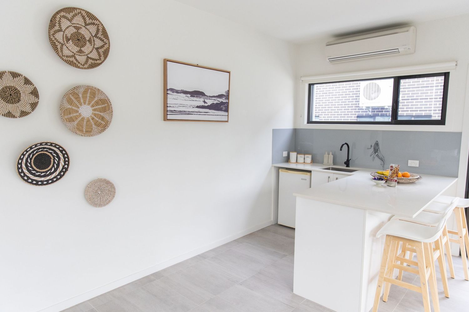 Minimalist white kitchen with decorative woven wall art and breakfast bar seating.