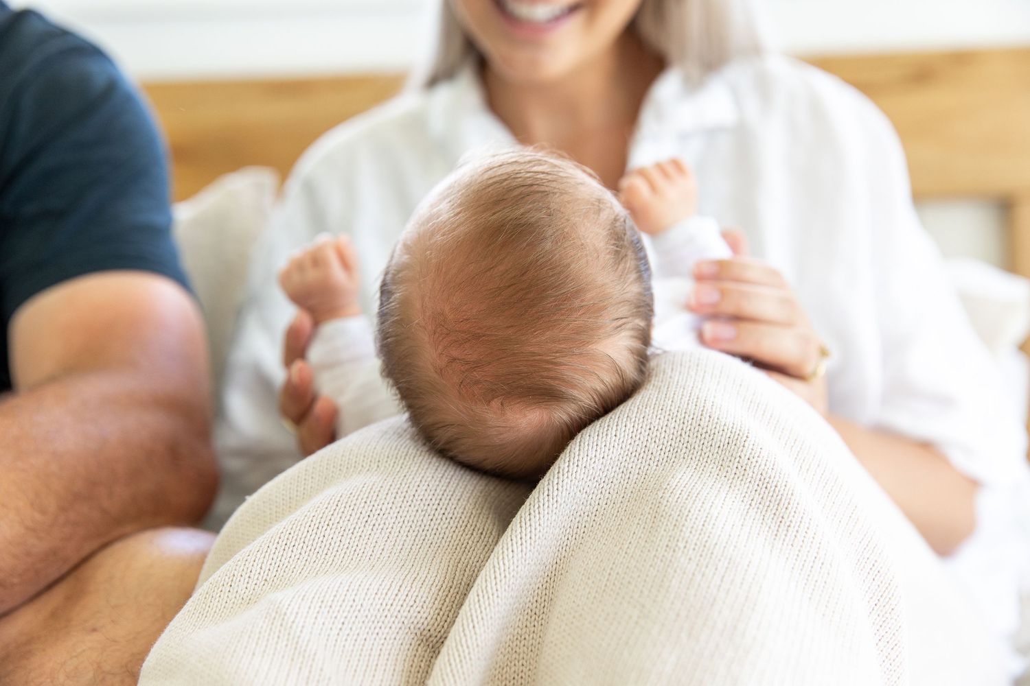 Tender moment between parents and newborn baby on white bedding.