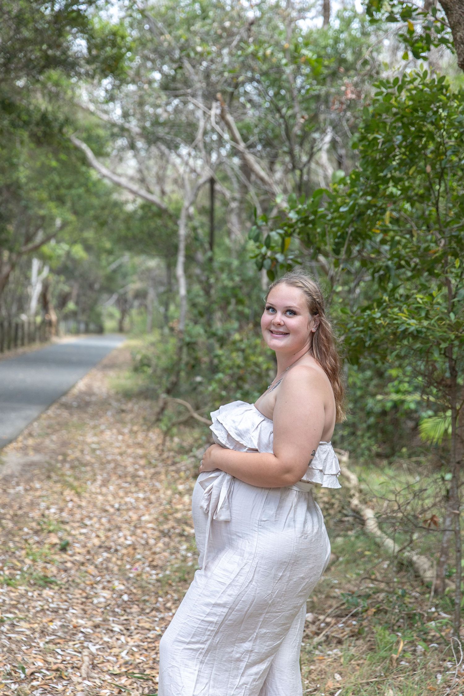 A person in a white dress poses playfully in a wooded outdoor setting with natural lighting.