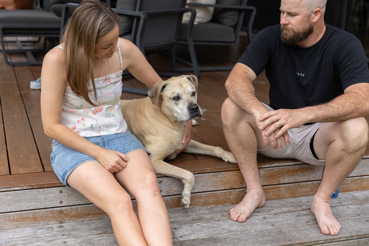 Family relaxing together on a wooden deck with their dog on a sunny day.