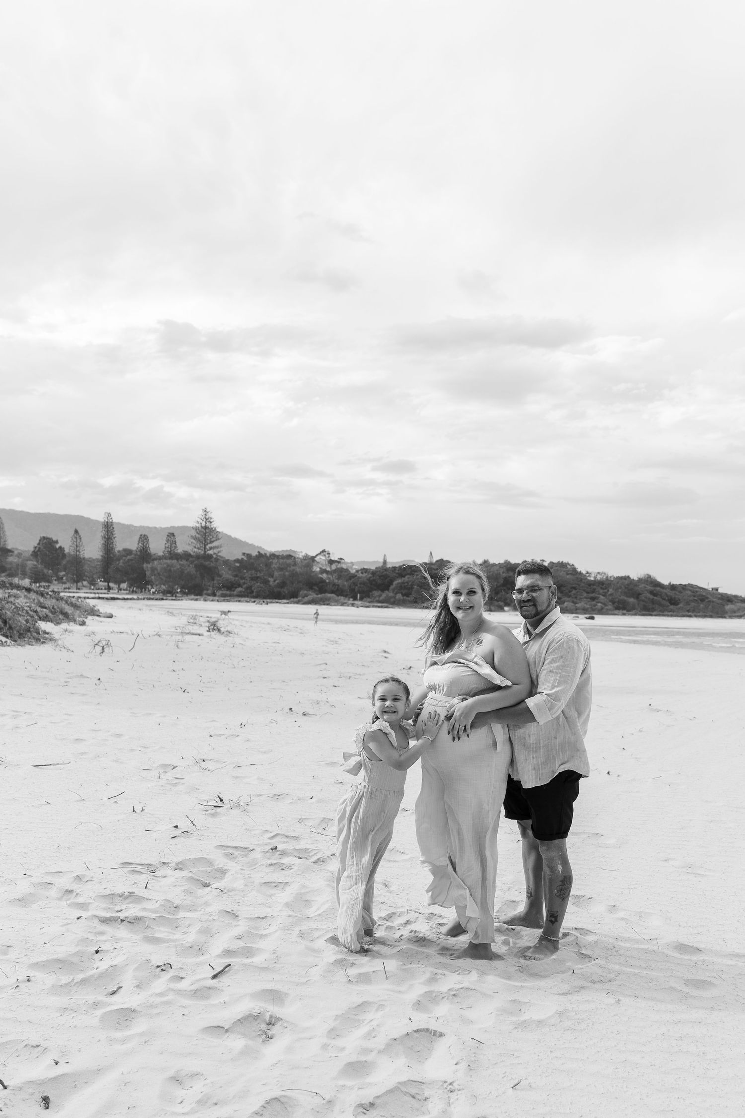 Family enjoying a playful moment together on a cloudy beach in black and white.