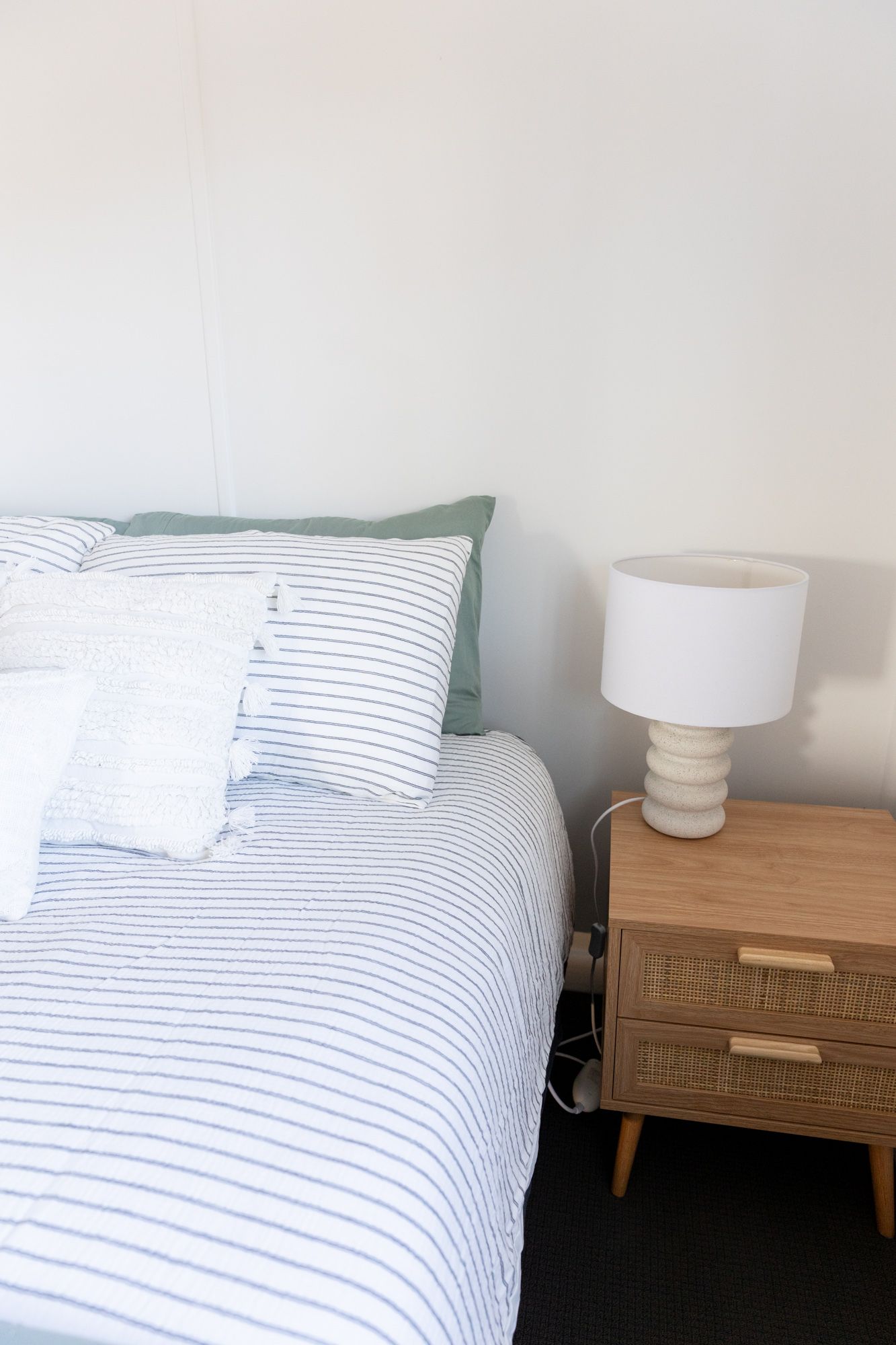 Minimalist bedroom with striped bedding, wooden nightstand, and white table lamp.