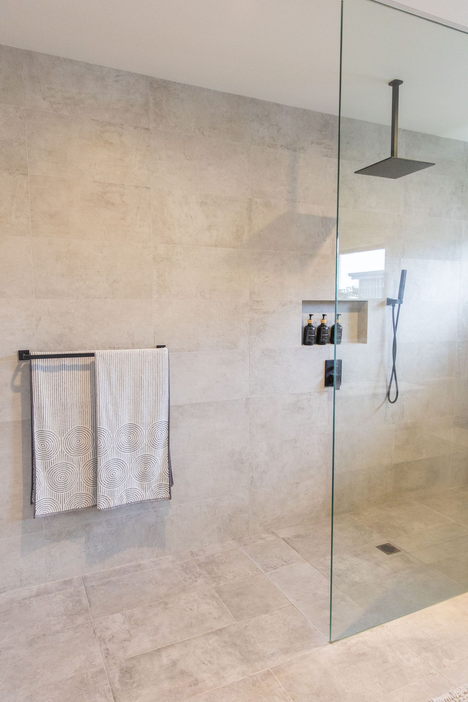 Modern bathroom featuring a glass shower enclosure and beige stone-look tile walls.